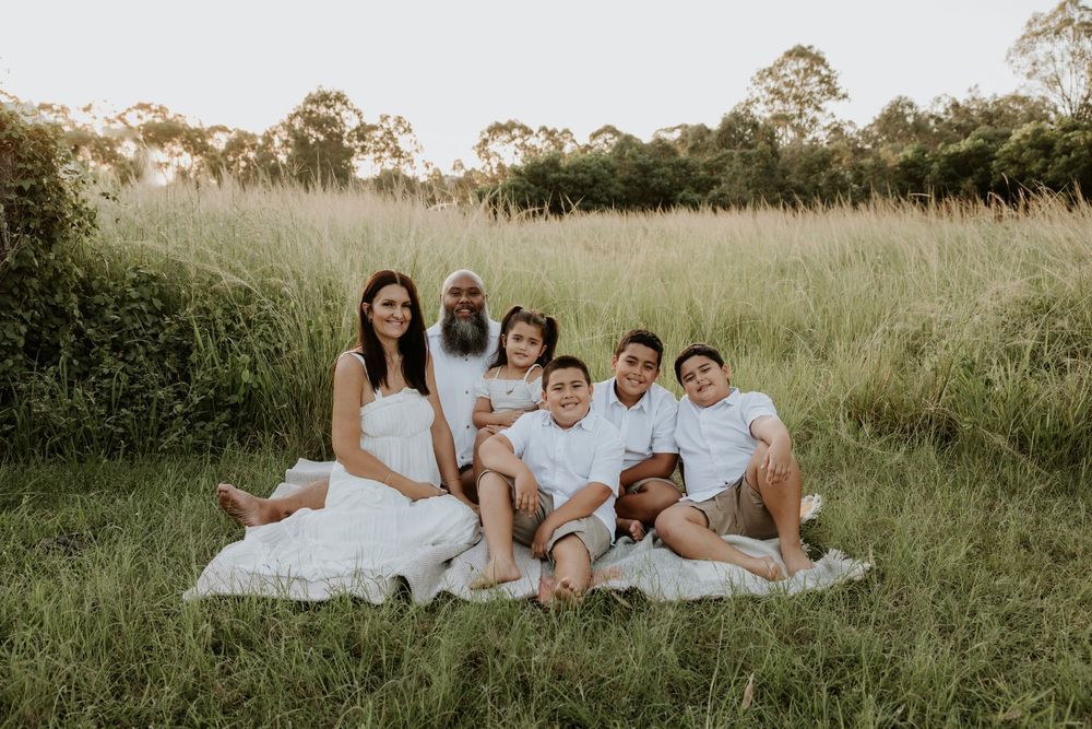 Family group relaxes together on grass during golden hour photo session in coordinated outfits.