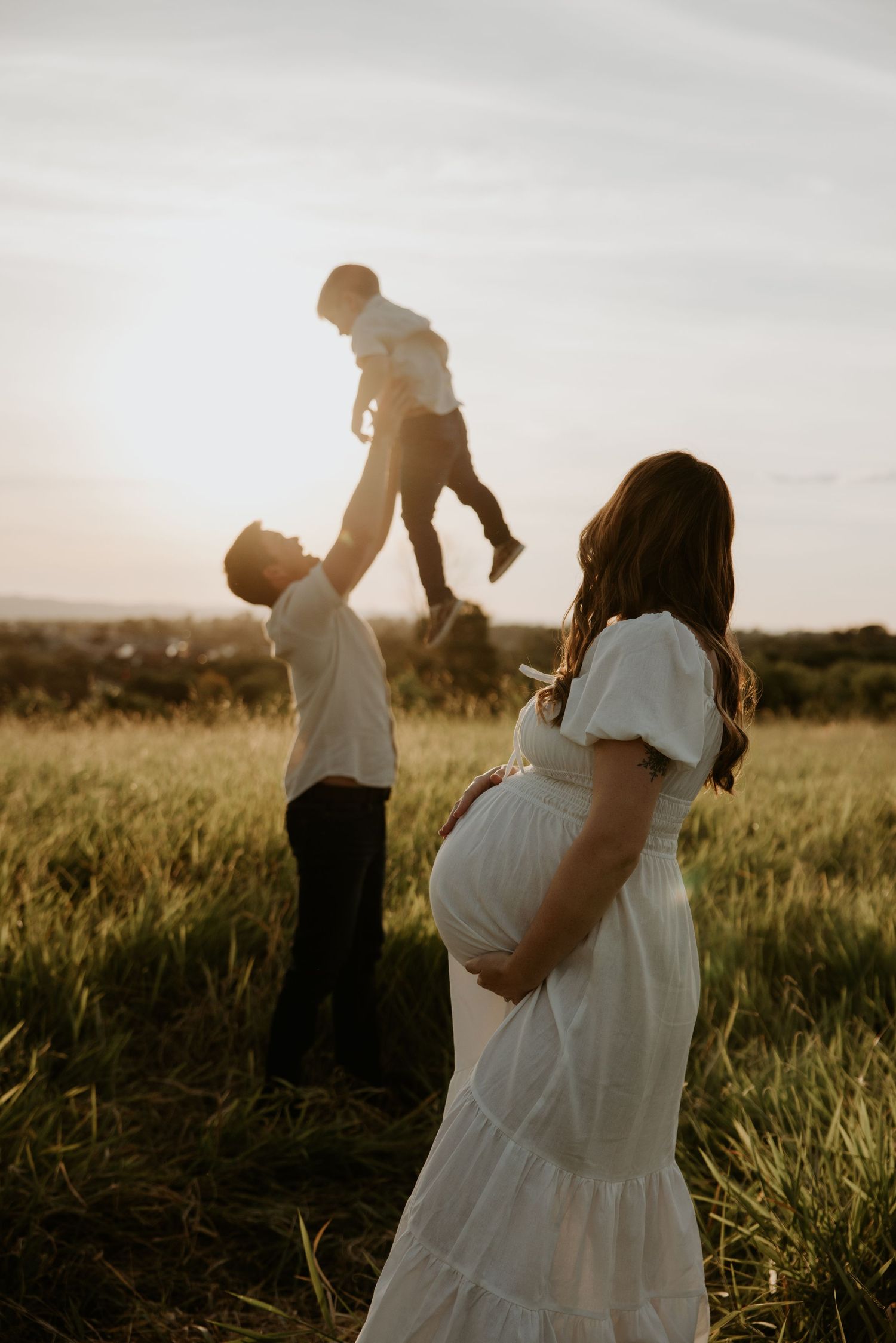 Family playing together in tall grass field during sunset.