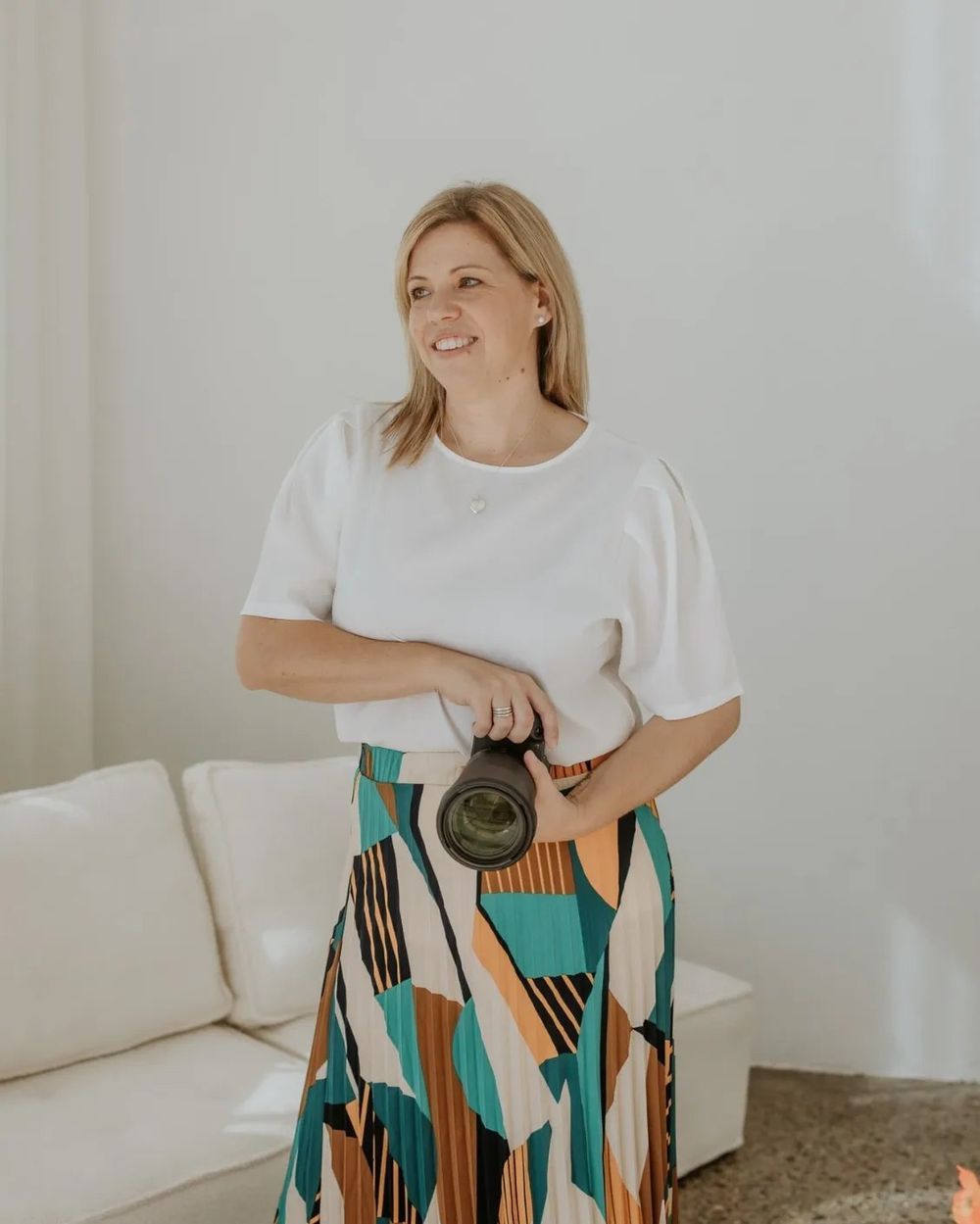 Woman in casual white top and colorful printed skirt posing in bright interior setting.