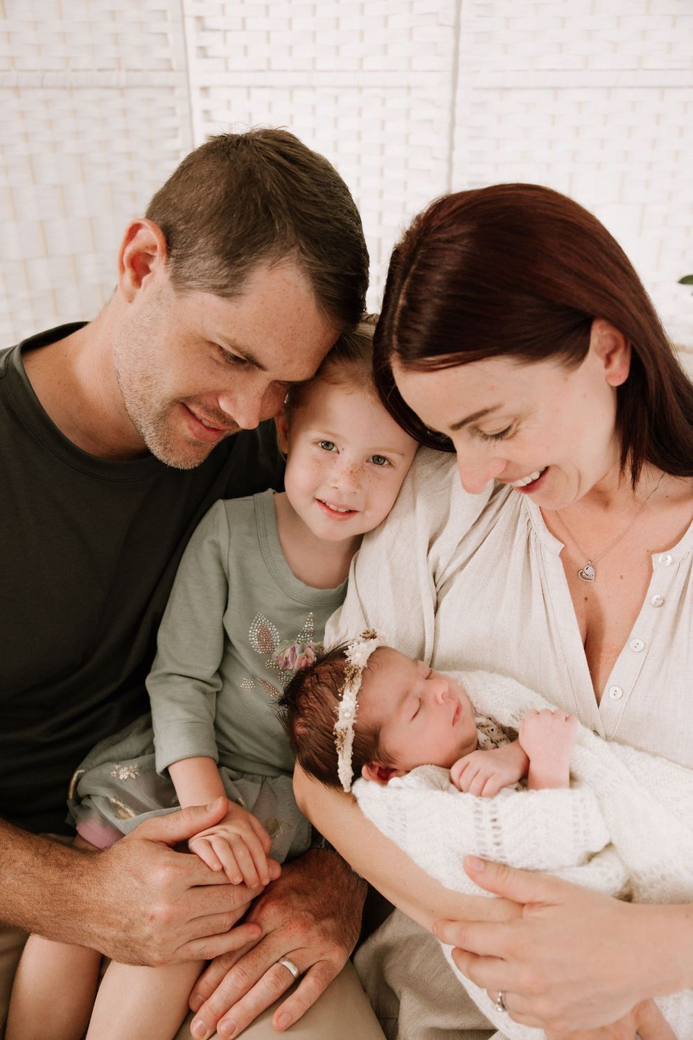 Family gathered together looking lovingly at newborn baby in white room.