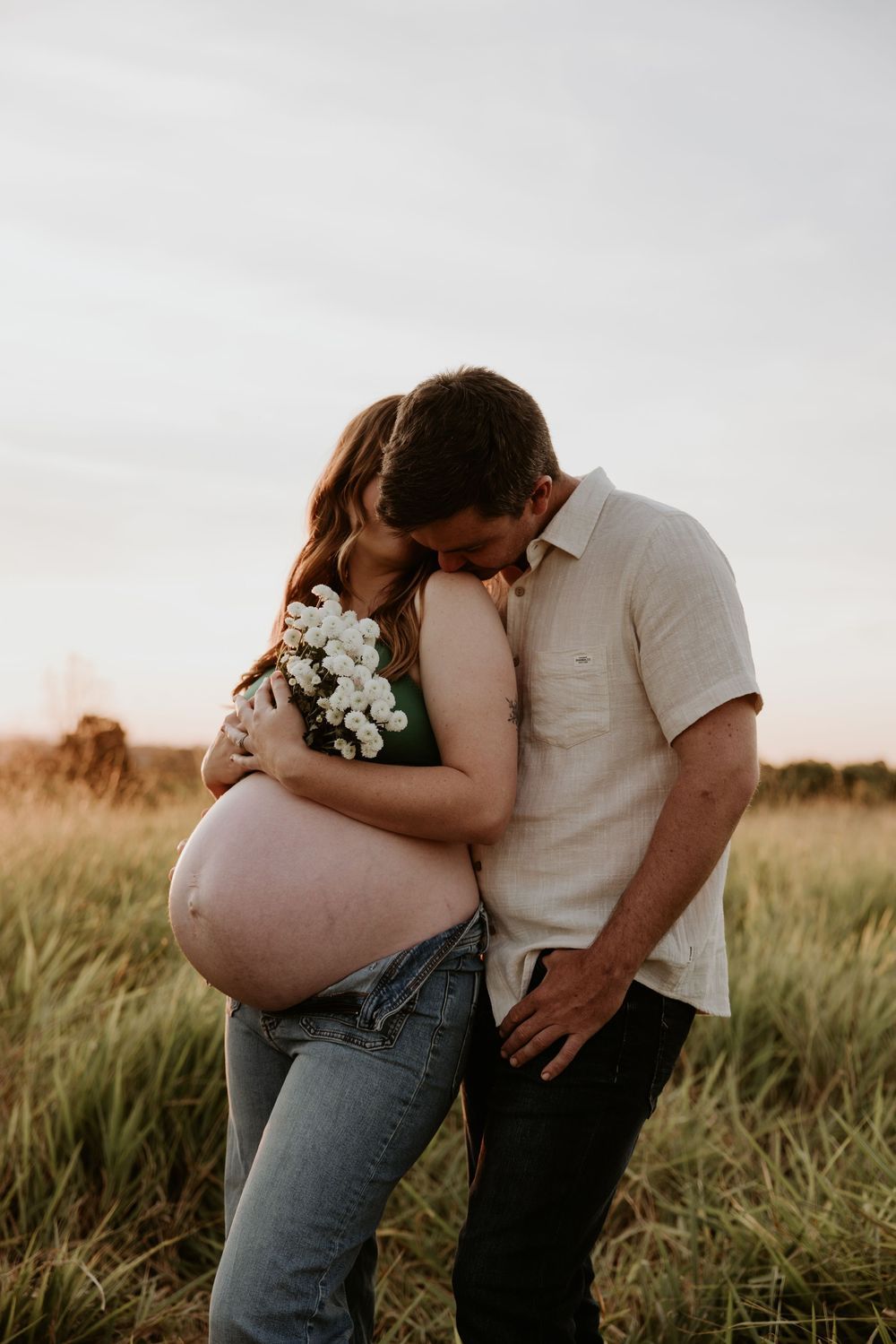 Couple sharing intimate moment in field during golden hour photography session.