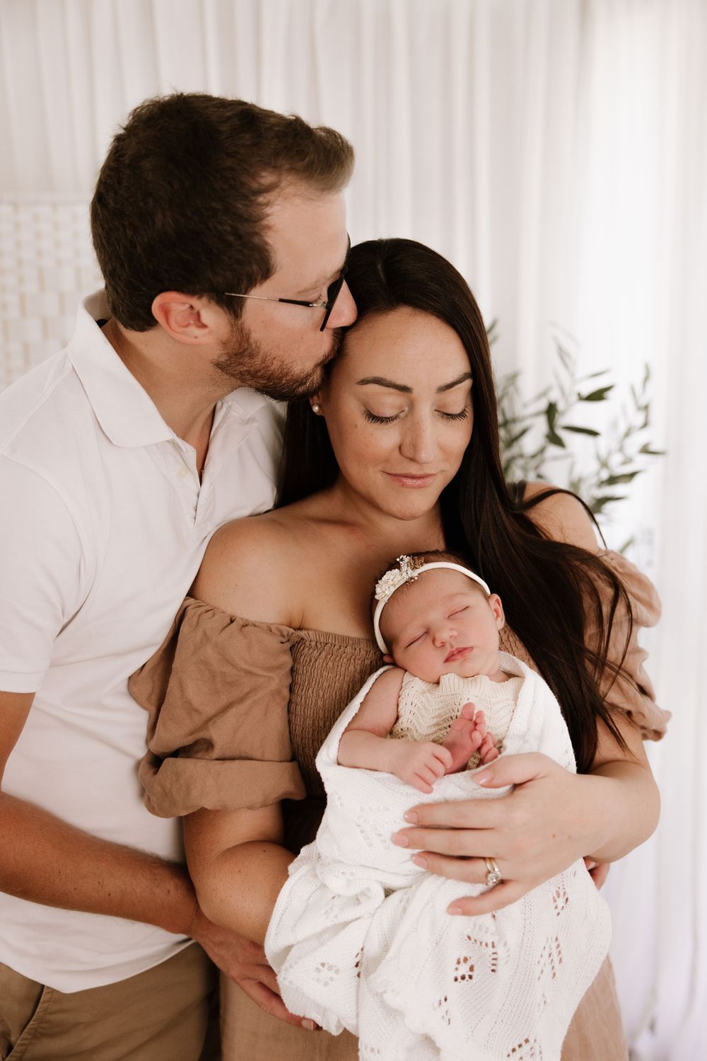 Intimate family moment with newborn baby in white dress being held and cuddled.