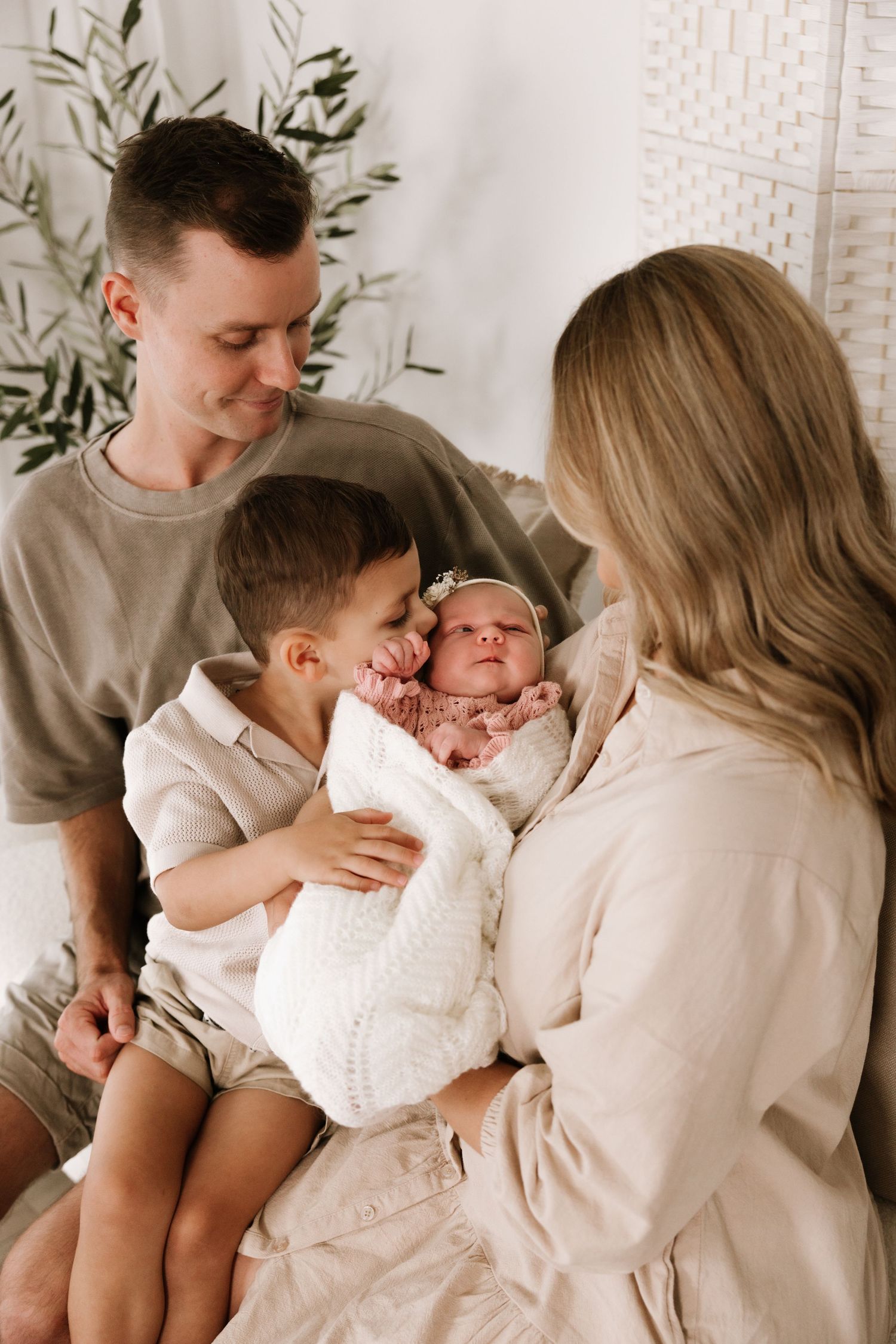 A young family admires their newborn baby girl, with dad, toddler son, and mom gathered closely together in a bright studio.