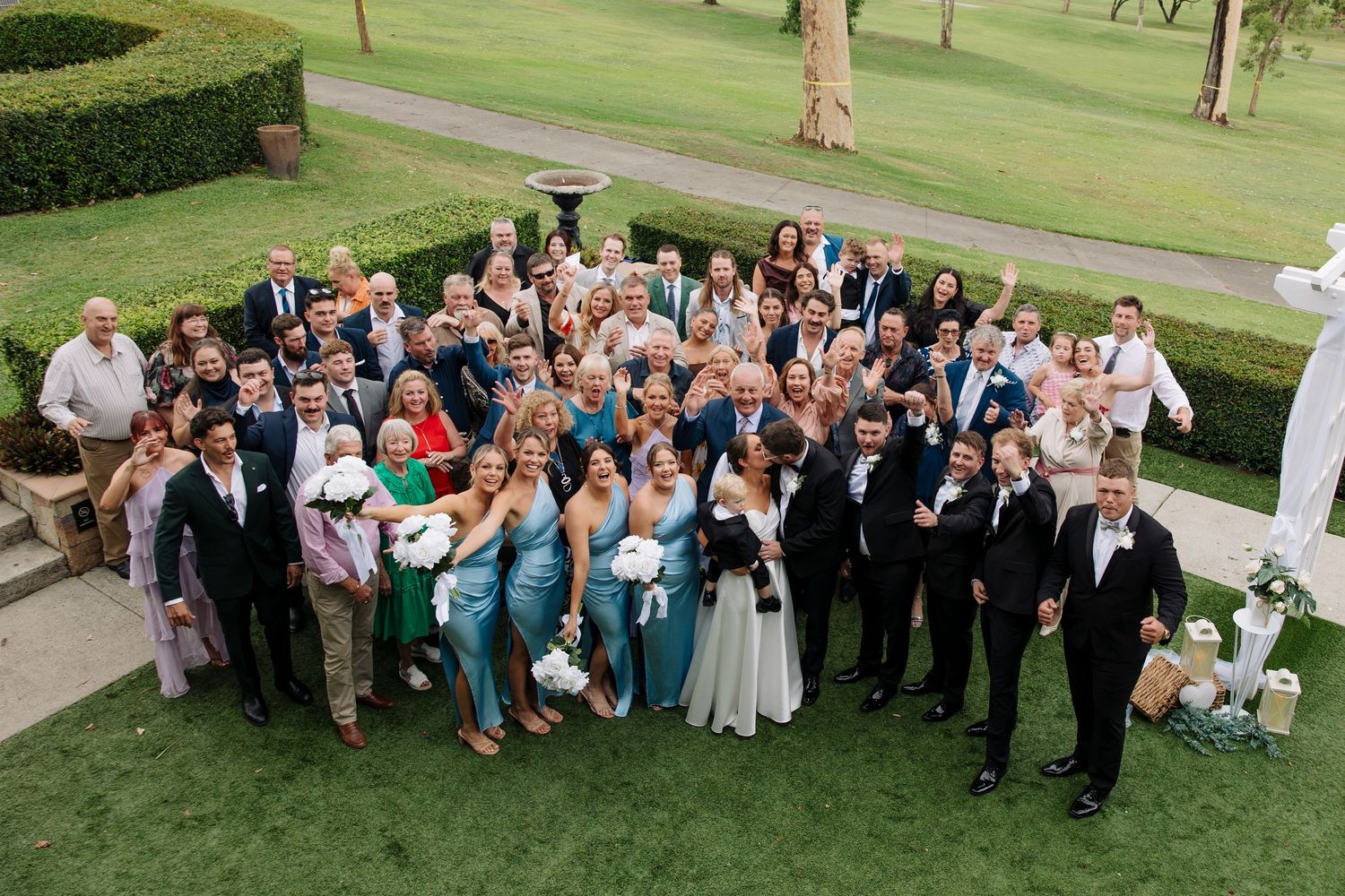 Large group wedding photo of guests and wedding party on green lawn.