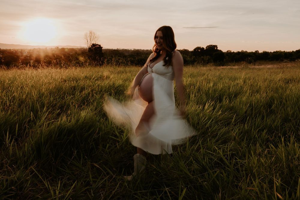 Ethereal sunset maternity photos in flowing white dress against golden field.