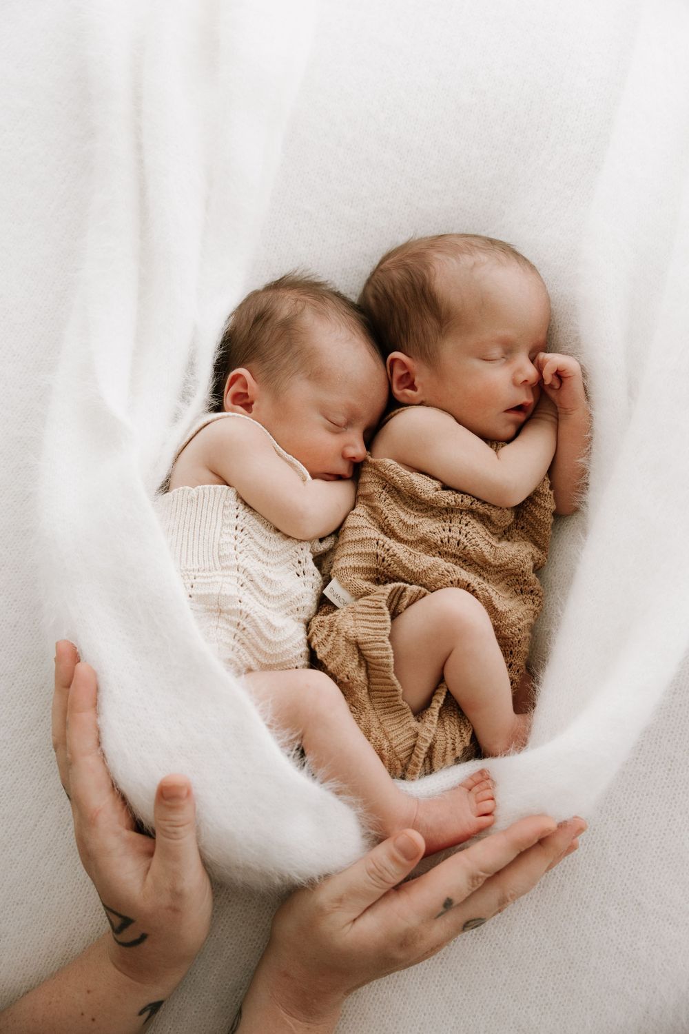 Two sleeping newborn babies nestled together on soft white fabric.