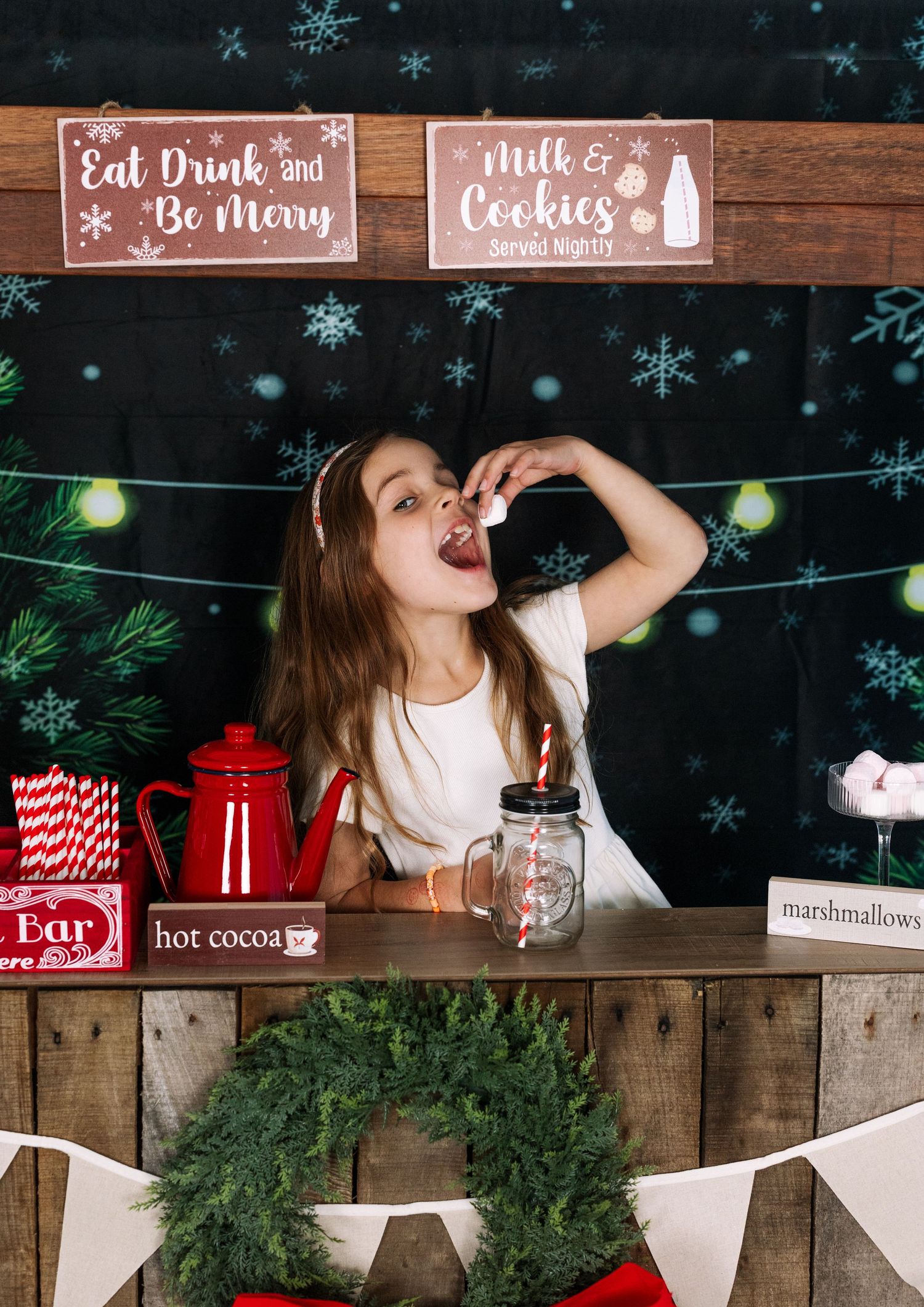 Children enjoy hot cocoa and treats at Christmas-themed photo booth with rustic decorations.