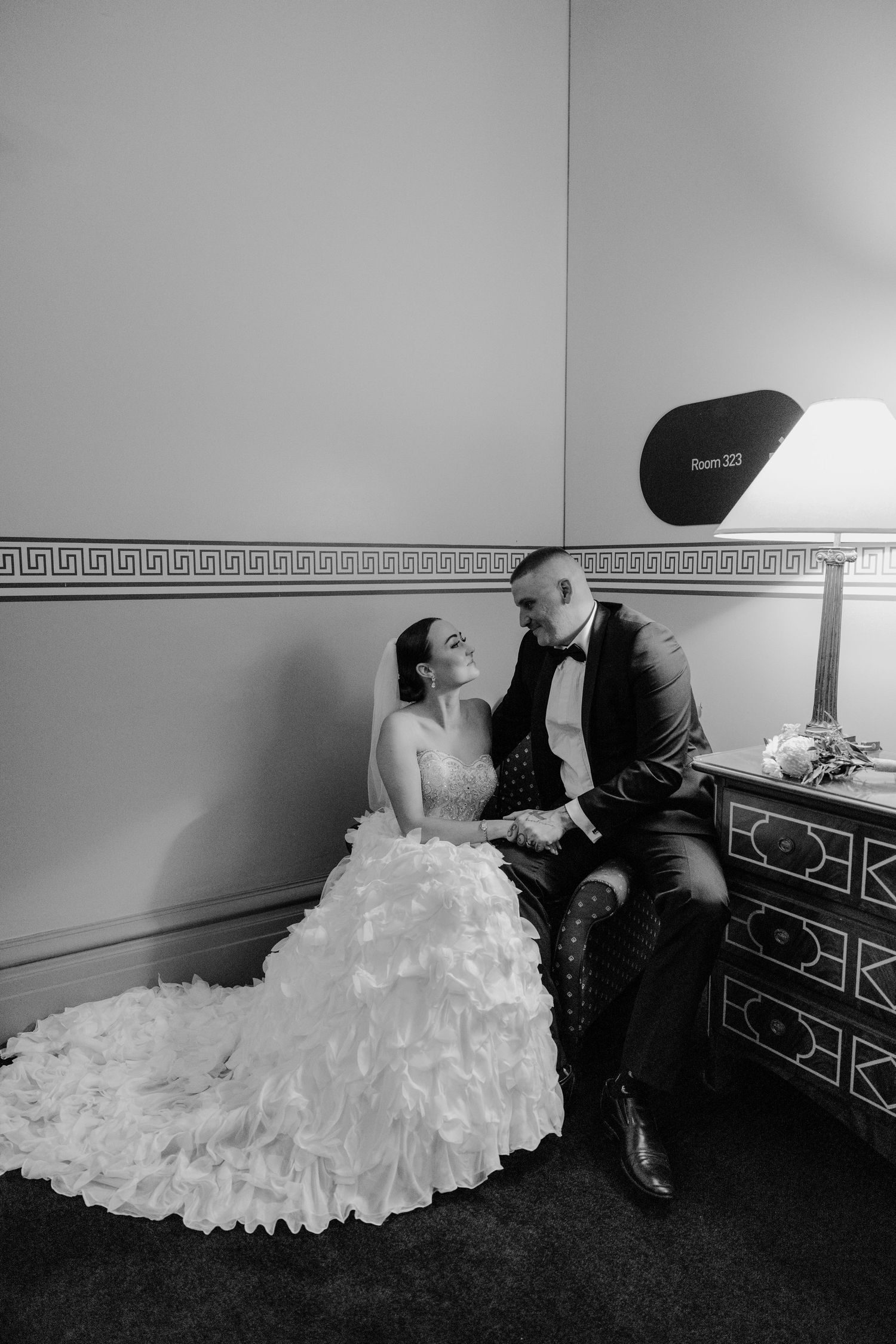 Black and white photo of couple in formal attire sitting on antique dresser.