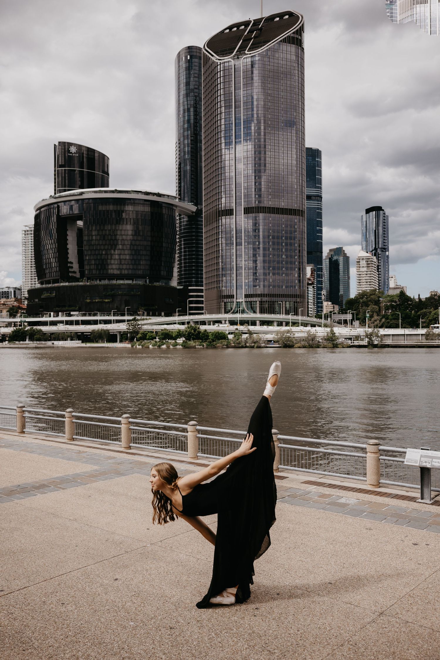 Dramatic dance pose against modern city architecture and riverfront.