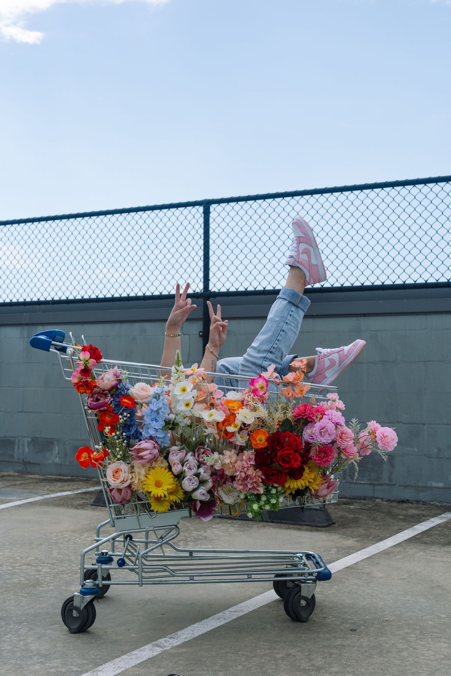 Creative photo with shopping cart filled with colorful flowers against urban backdrop.