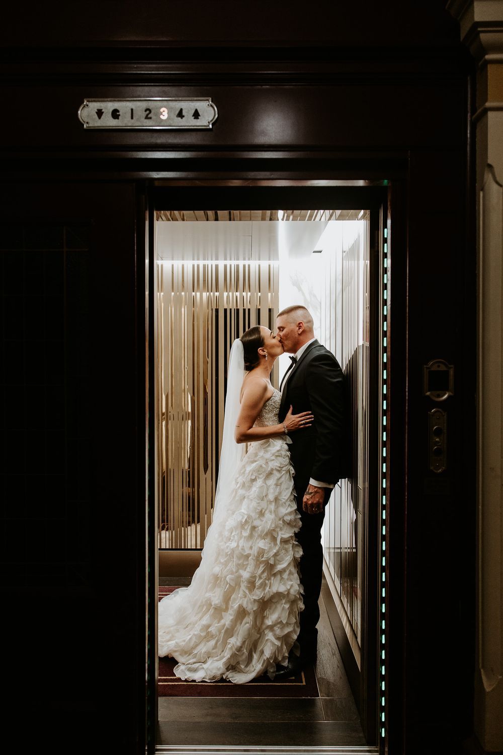 Wedding couple shares intimate moment in an elevator with dramatic lighting.