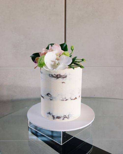Elegant white wedding cake with delicate floral decorations displayed on a clear acrylic stand.