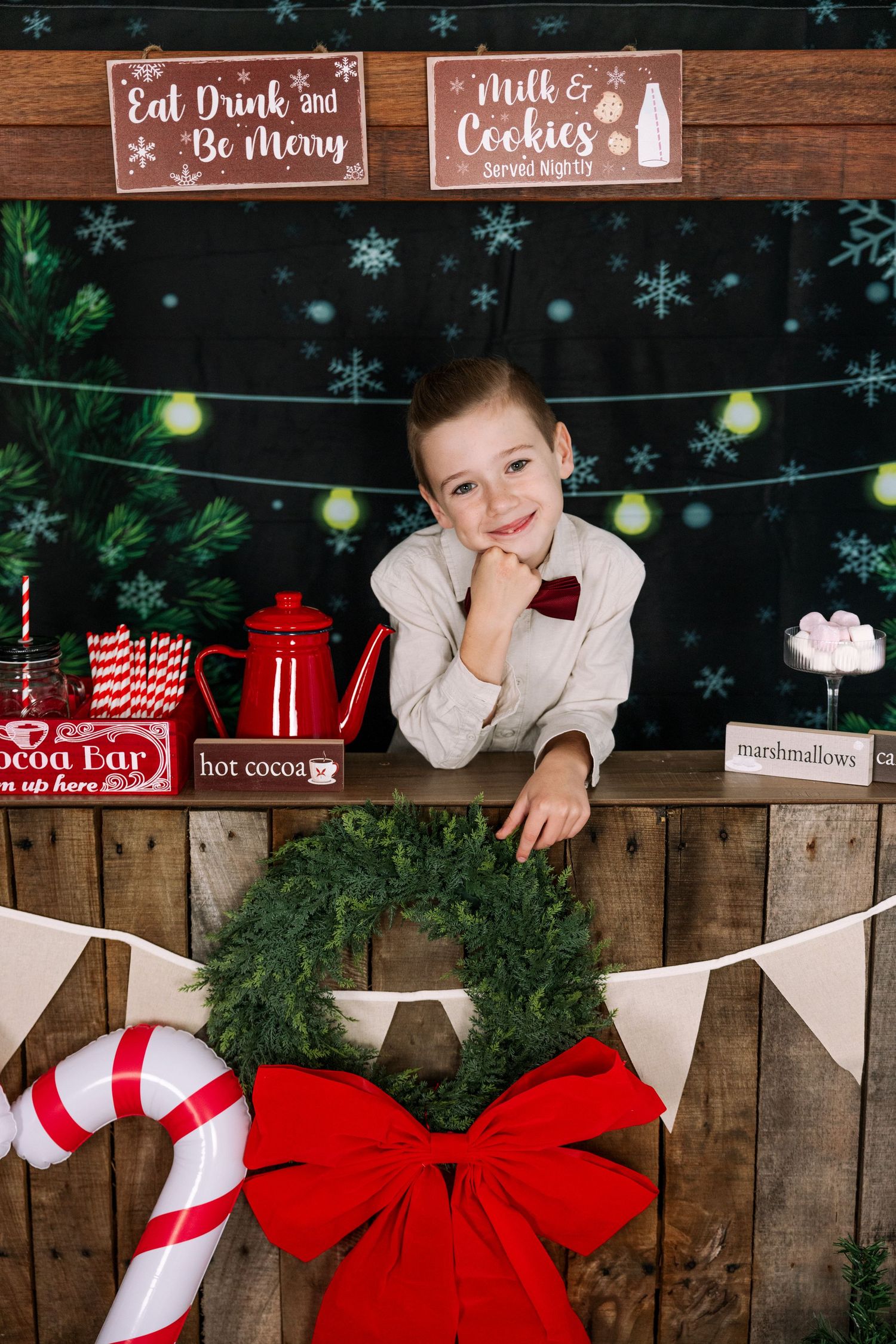 Rustic Christmas photo booth display with candy canes, wreaths and white bunting against wooden backdrop.