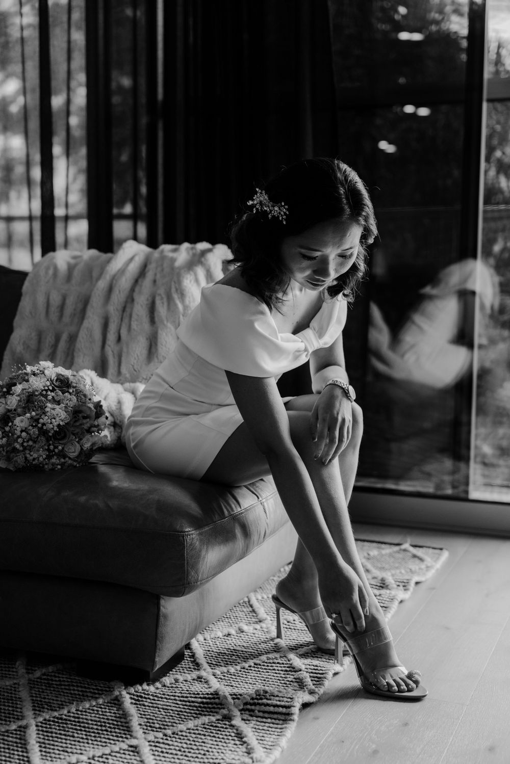 Black and white photo of someone sitting on a patterned rug reaching down to touch the floor.