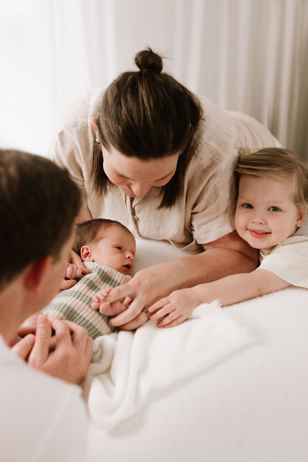 Intimate family lifestyle photos showing tender moments with baby on white bedding.