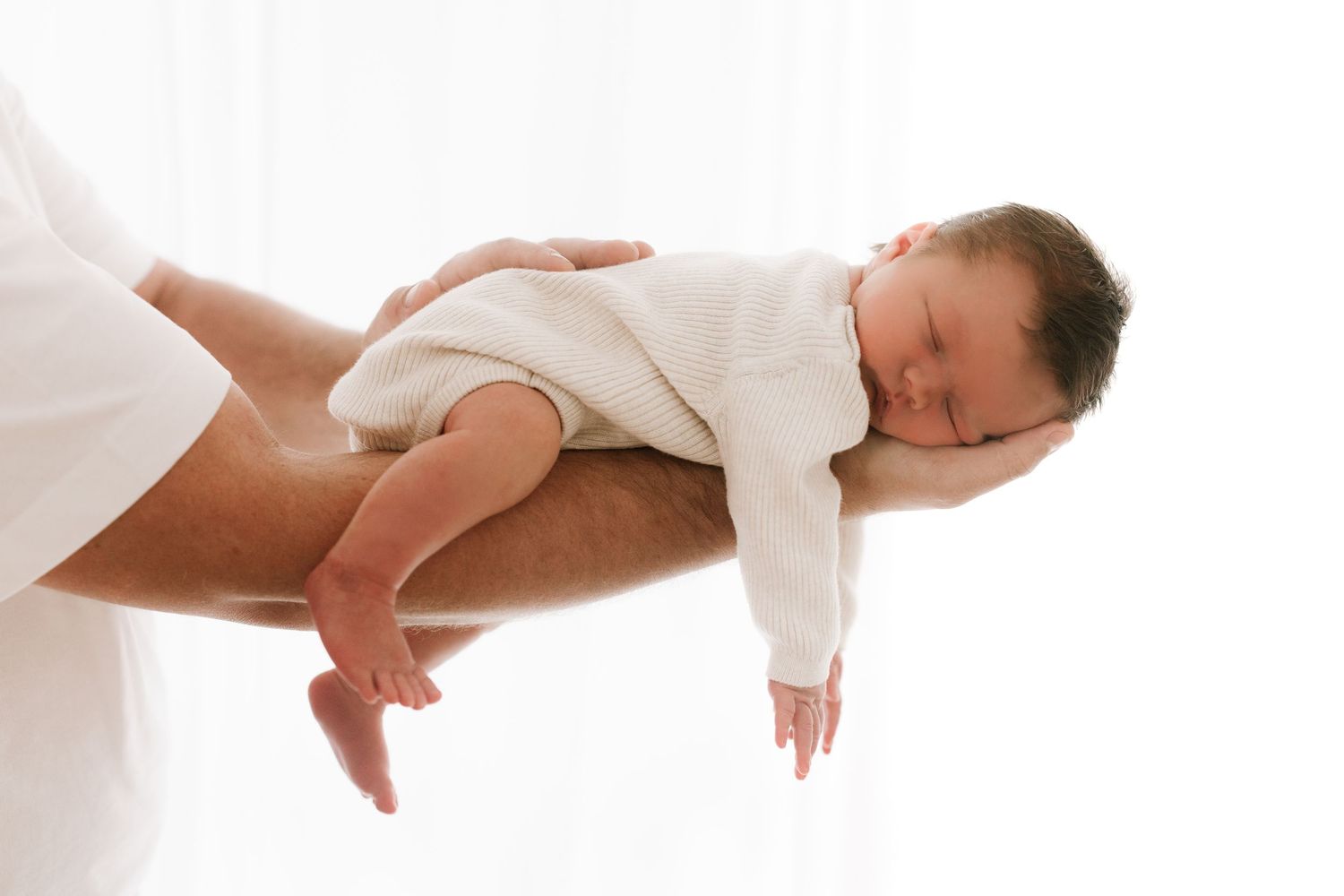 Peaceful sleeping newborn baby in white onesie cradled in arms.