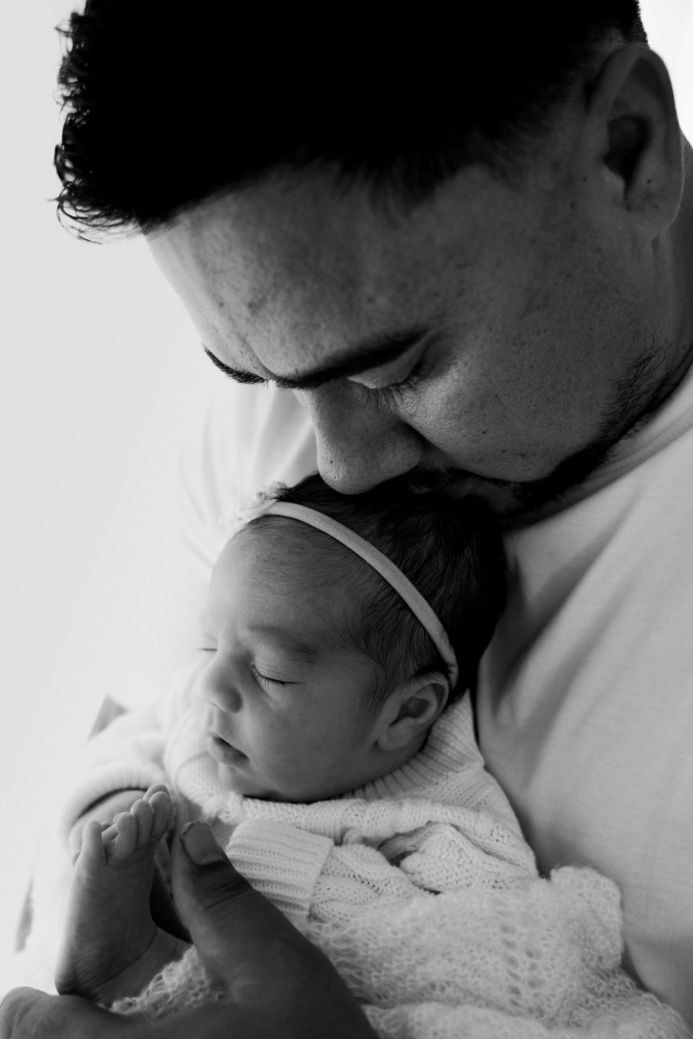 Parent sharing gentle moment with newborn baby in black and white portrait.