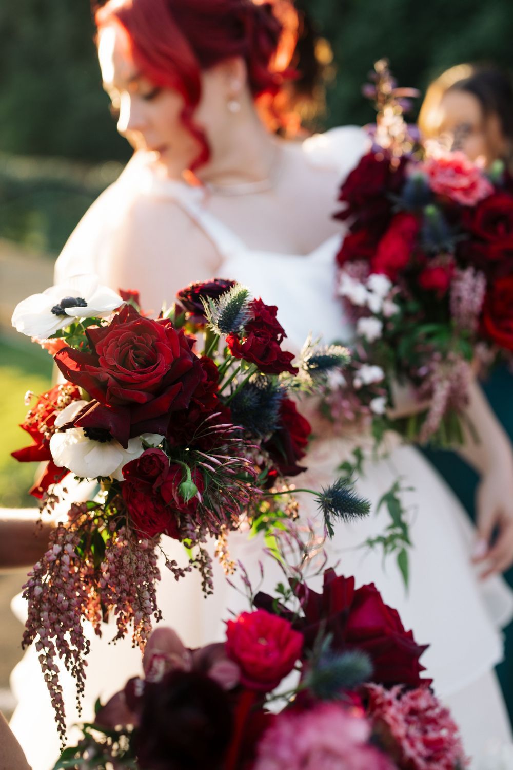 Deep red and burgundy wedding bouquets with roses and trailing foliage create a dramatic floral display.