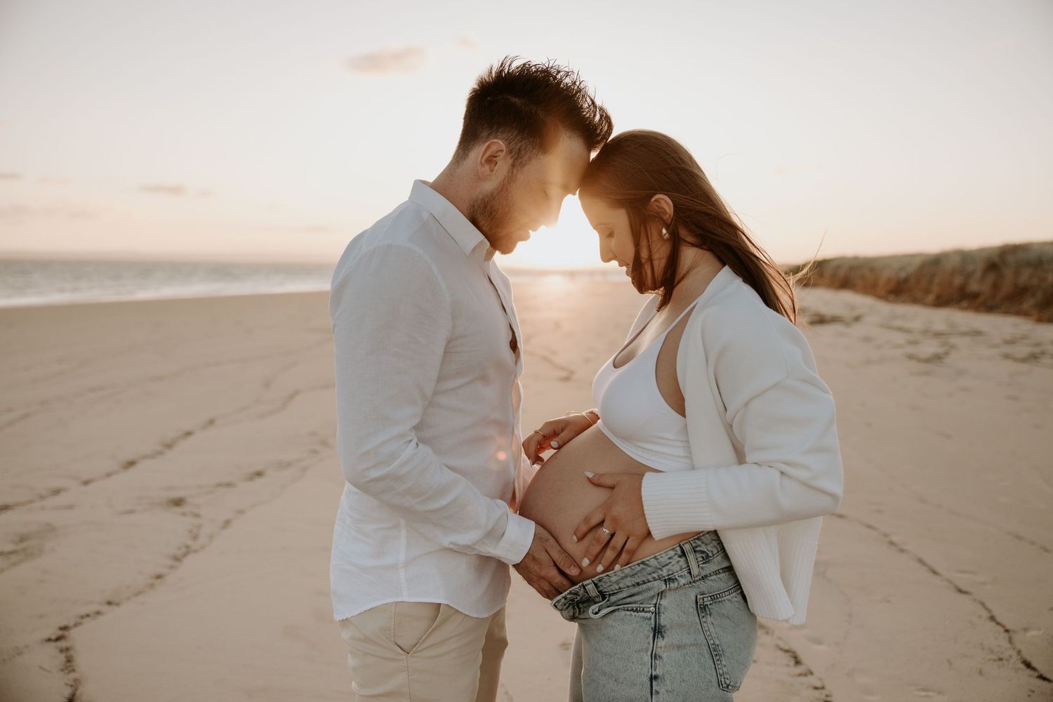 Casual couple embraces on sandy beach during sunset photoshoot.