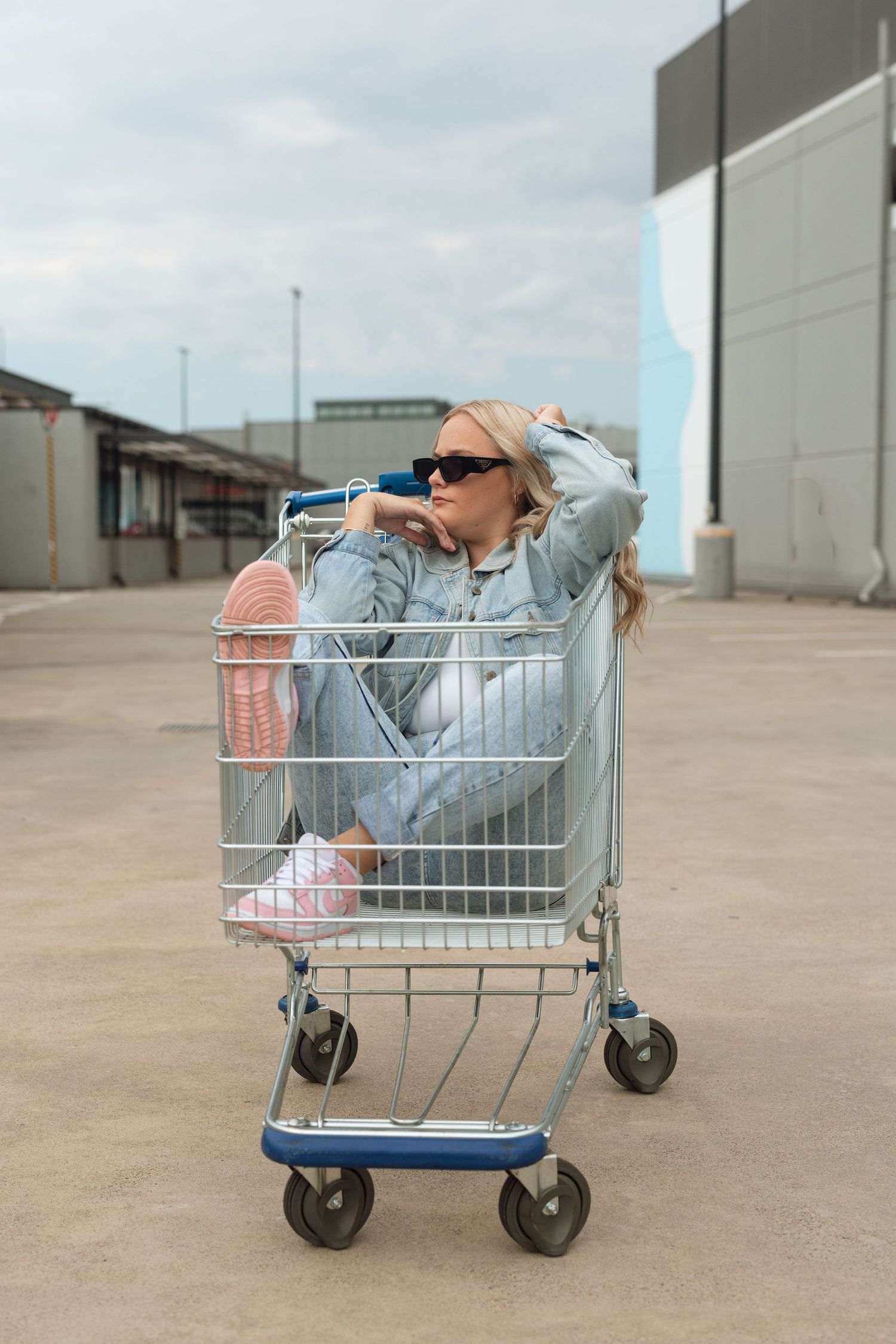 Artistic series of poses in shopping cart against industrial backdrop.