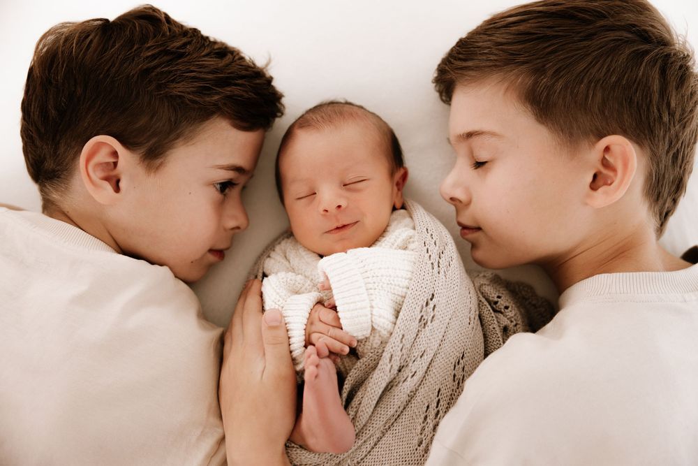 Series of siblings lying together on white bedding showing gentle interaction with newborn.