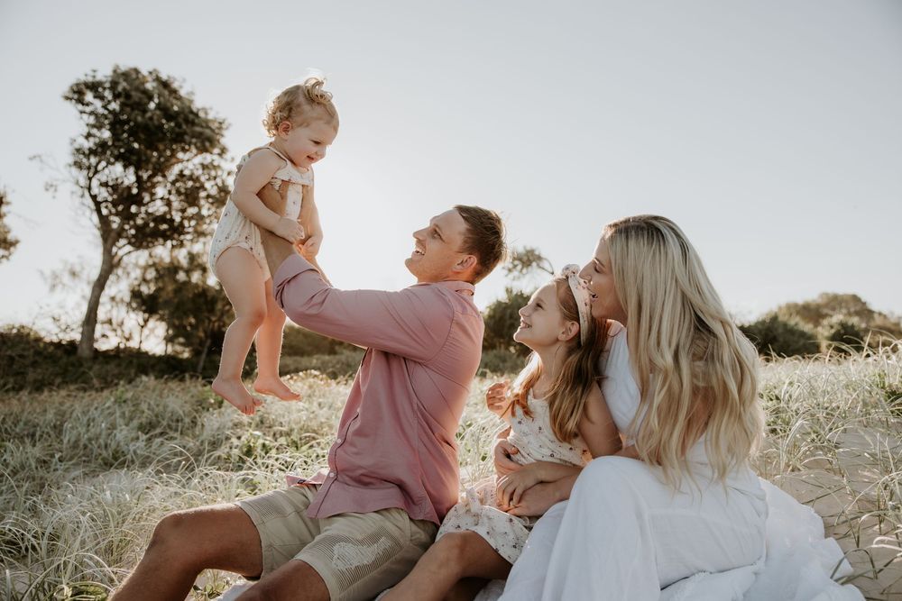 Family portrait session in a sunlit field with golden light filtering through trees.