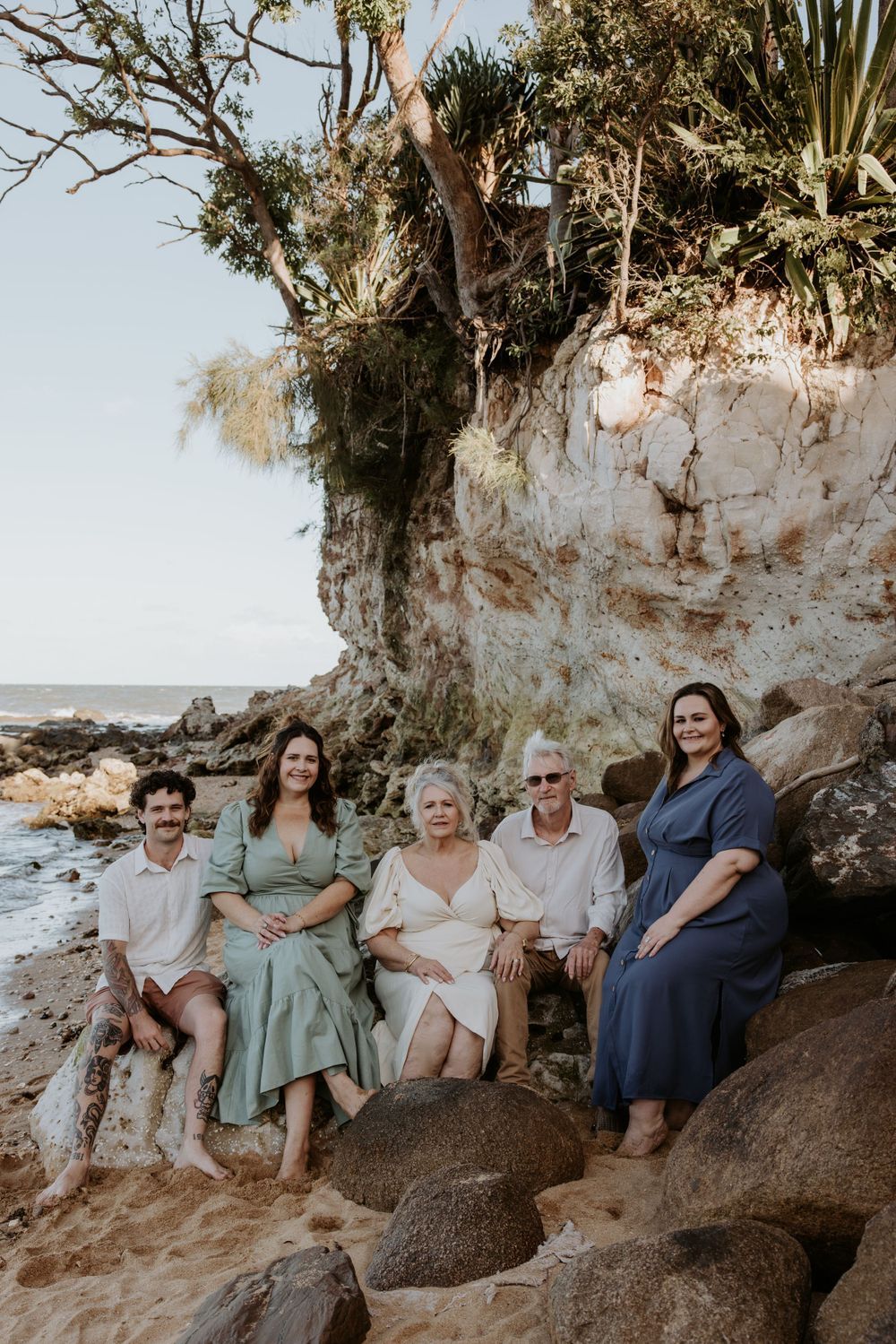 Group relaxes on rocky coastal outcrop during sunset photo session wearing coordinated casual attire.