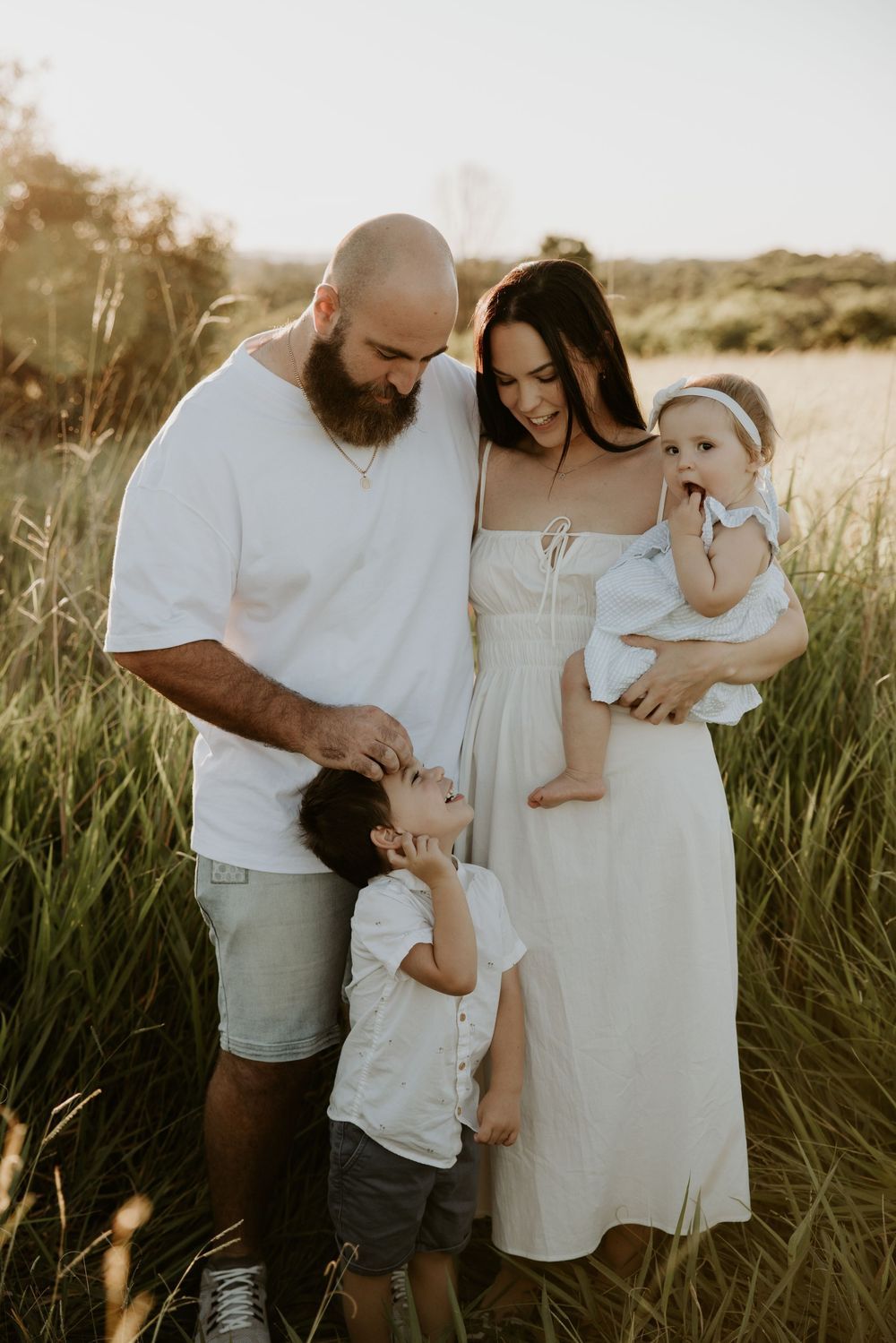Intimate family moment captured in tall grass during golden hour with soft natural lighting.