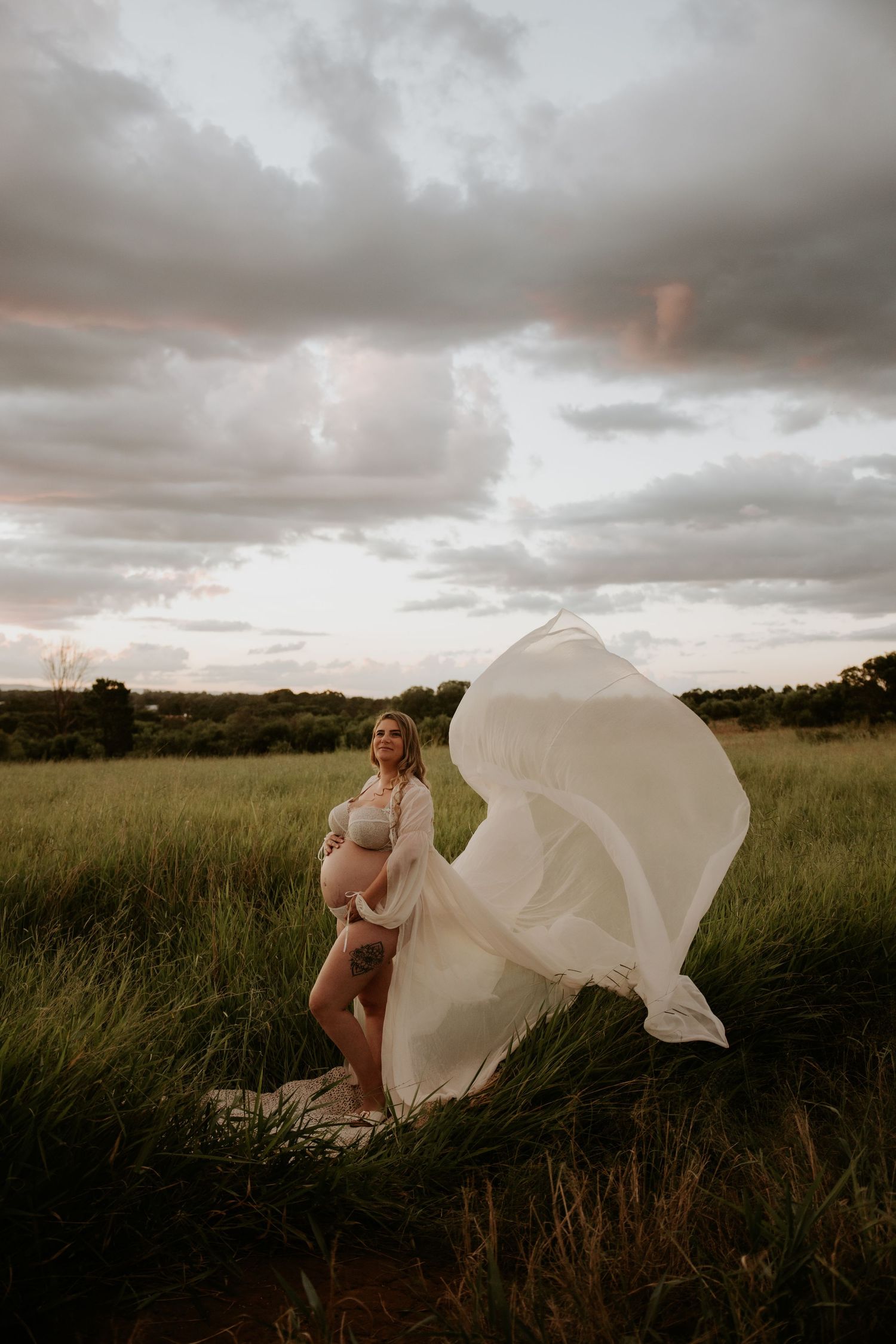 Dramatic portrait session in field with flowing white dress against stormy sky.
