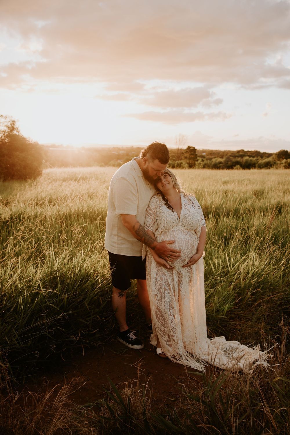 Romantic sunset maternity photos in a grassy field with couple in white clothing.