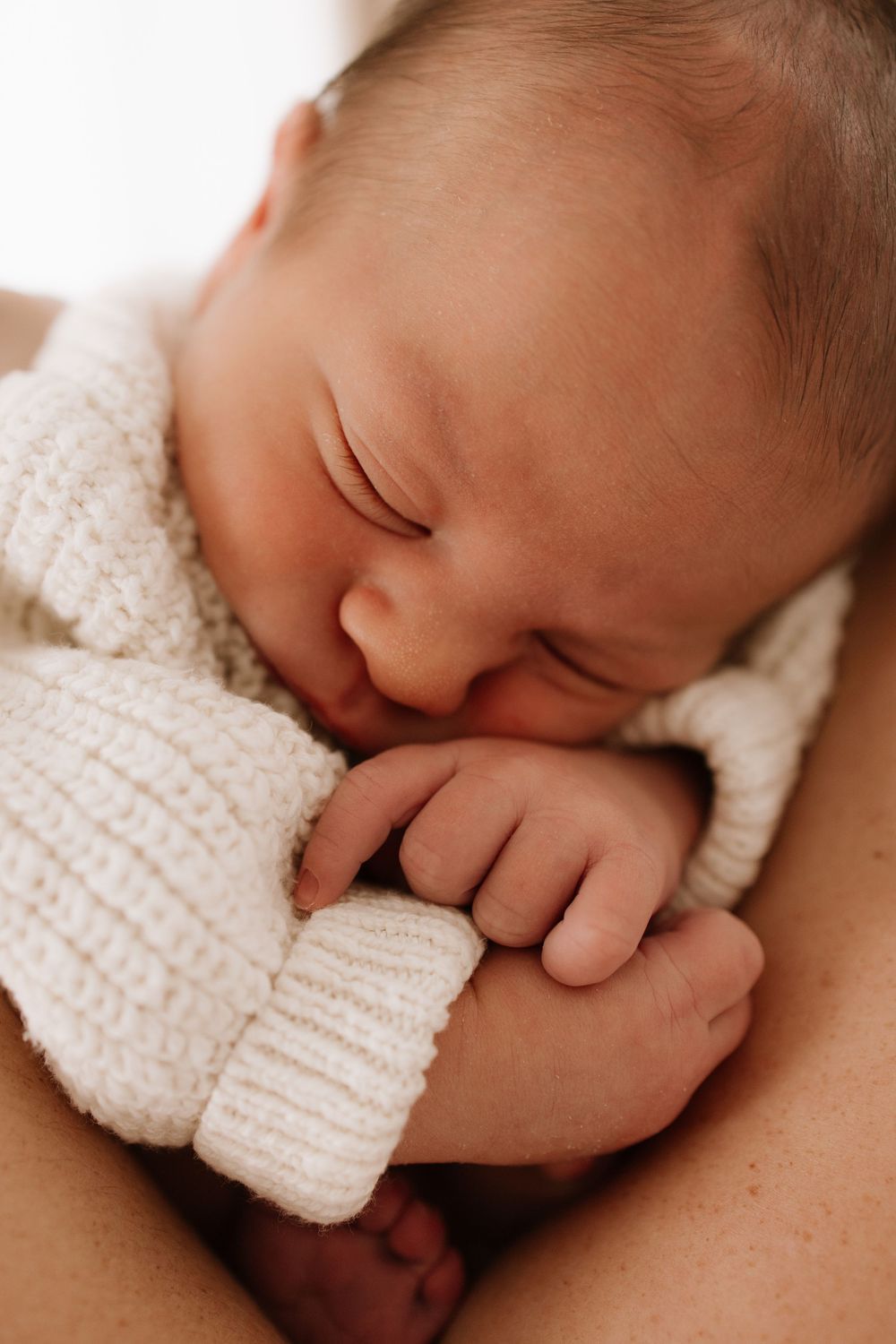 Close-up of newborn baby sleeping peacefully in soft cream knit blanket.