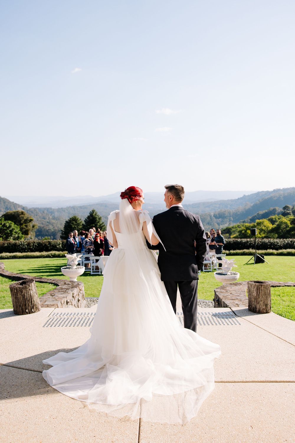 Newlyweds walk together on a scenic outdoor patio overlooking mountain views on their wedding day.