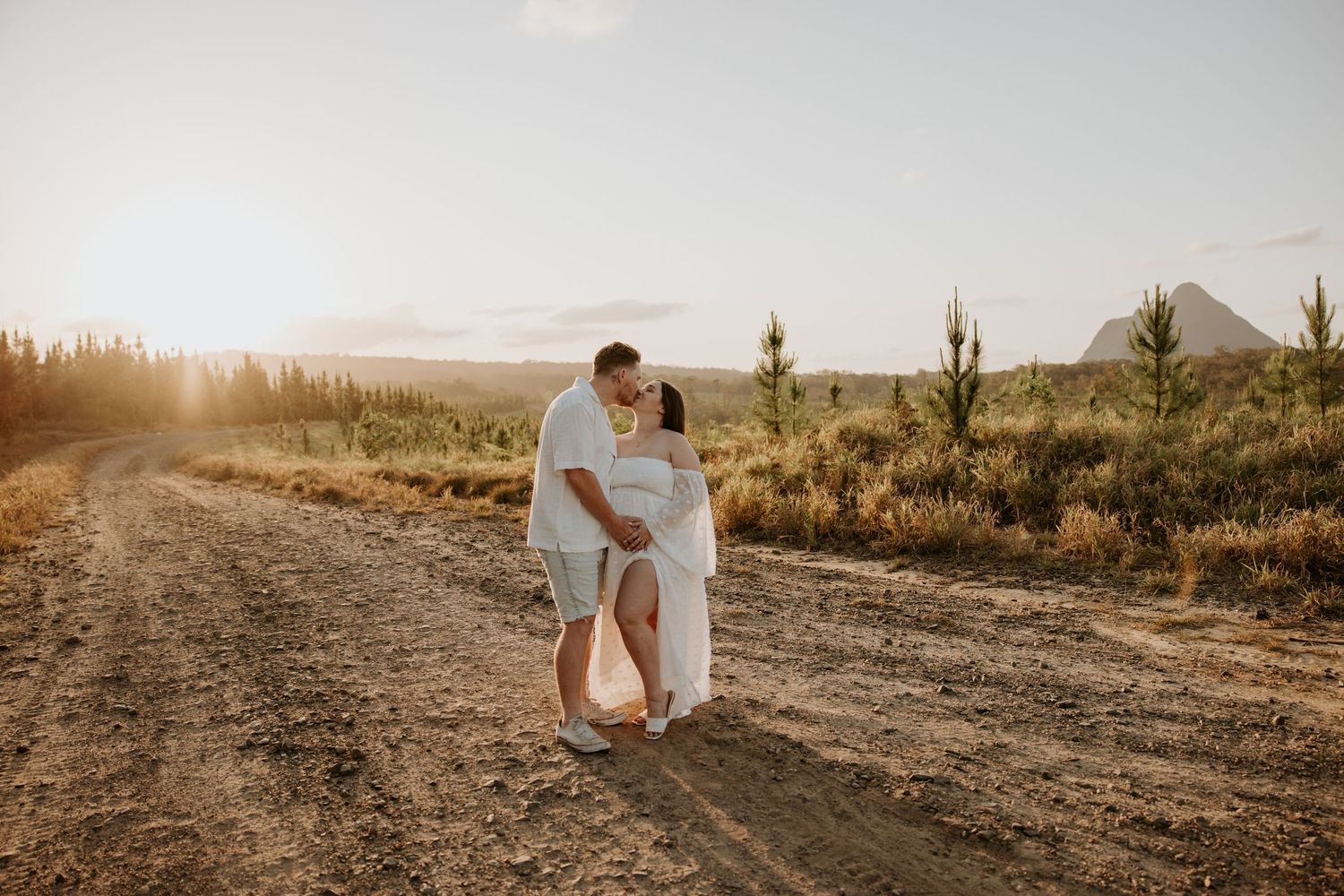 Couple embracing on dirt road with desert landscape at sunset.