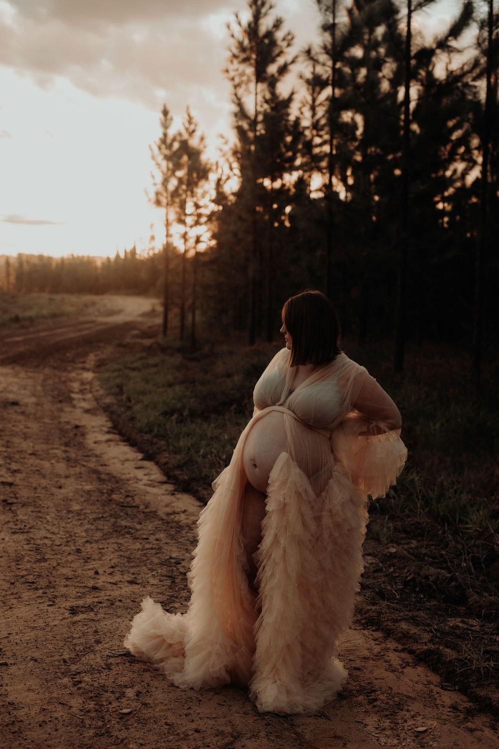 Silhouette of person in flowing dress against sunset and pine trees.