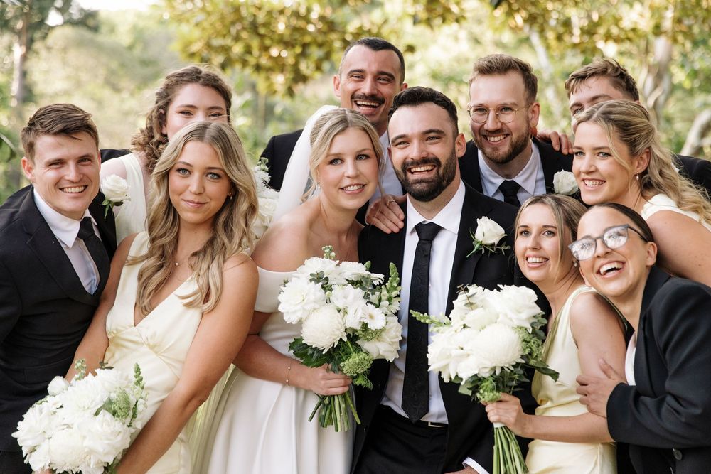 Wedding party laughing together outdoors with white floral bouquets.