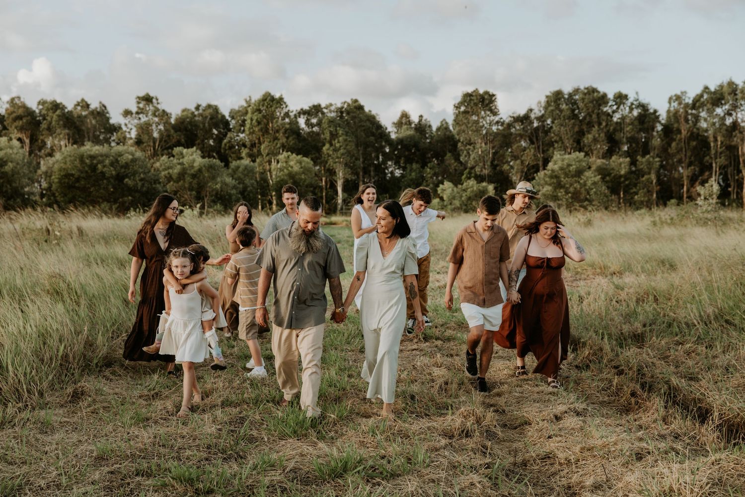 Large family group walking together through a scenic green meadow field during an outdoor photo session.