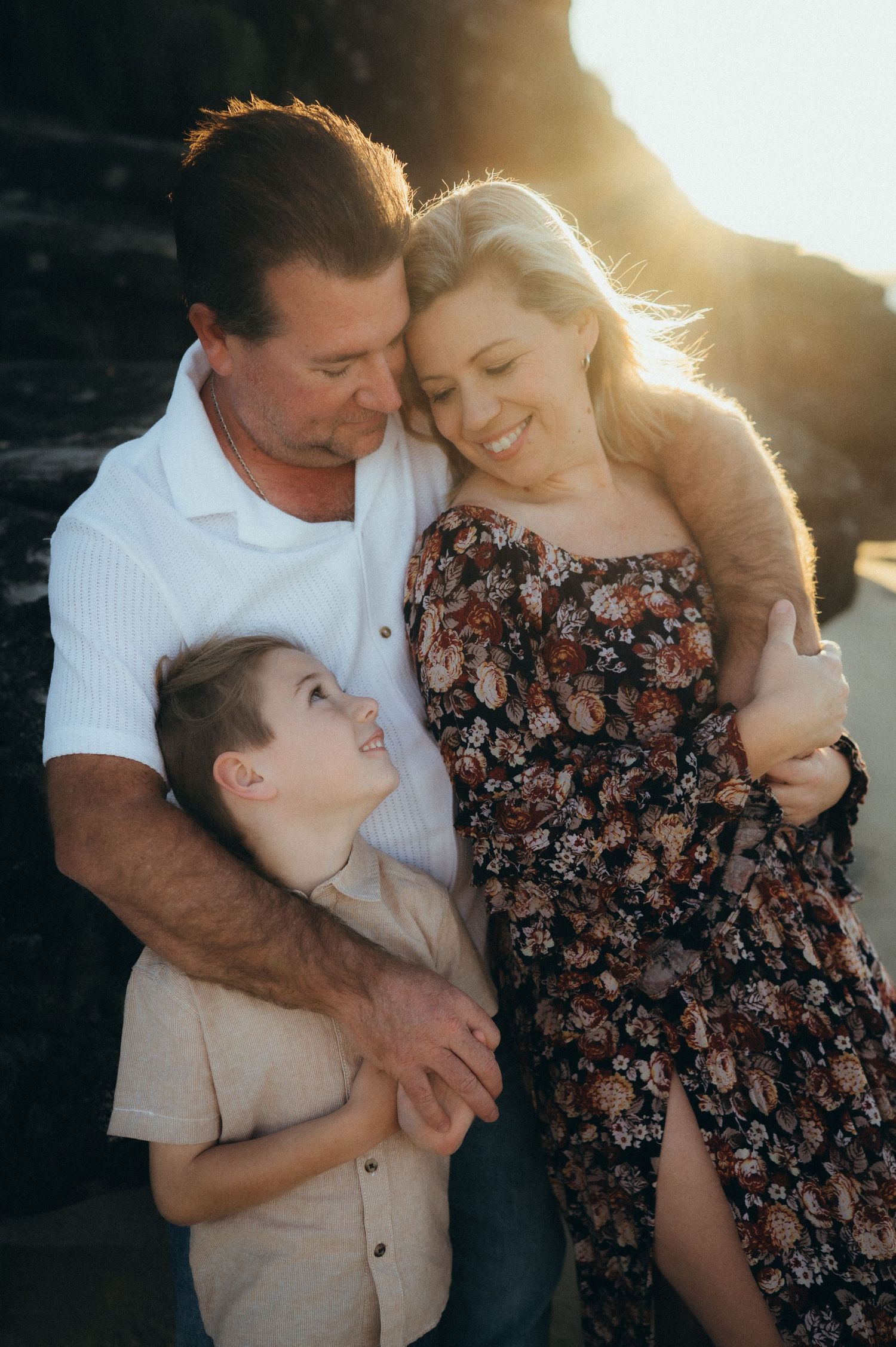 A tender family moment captured at sunset on rocky coastal cliffs.