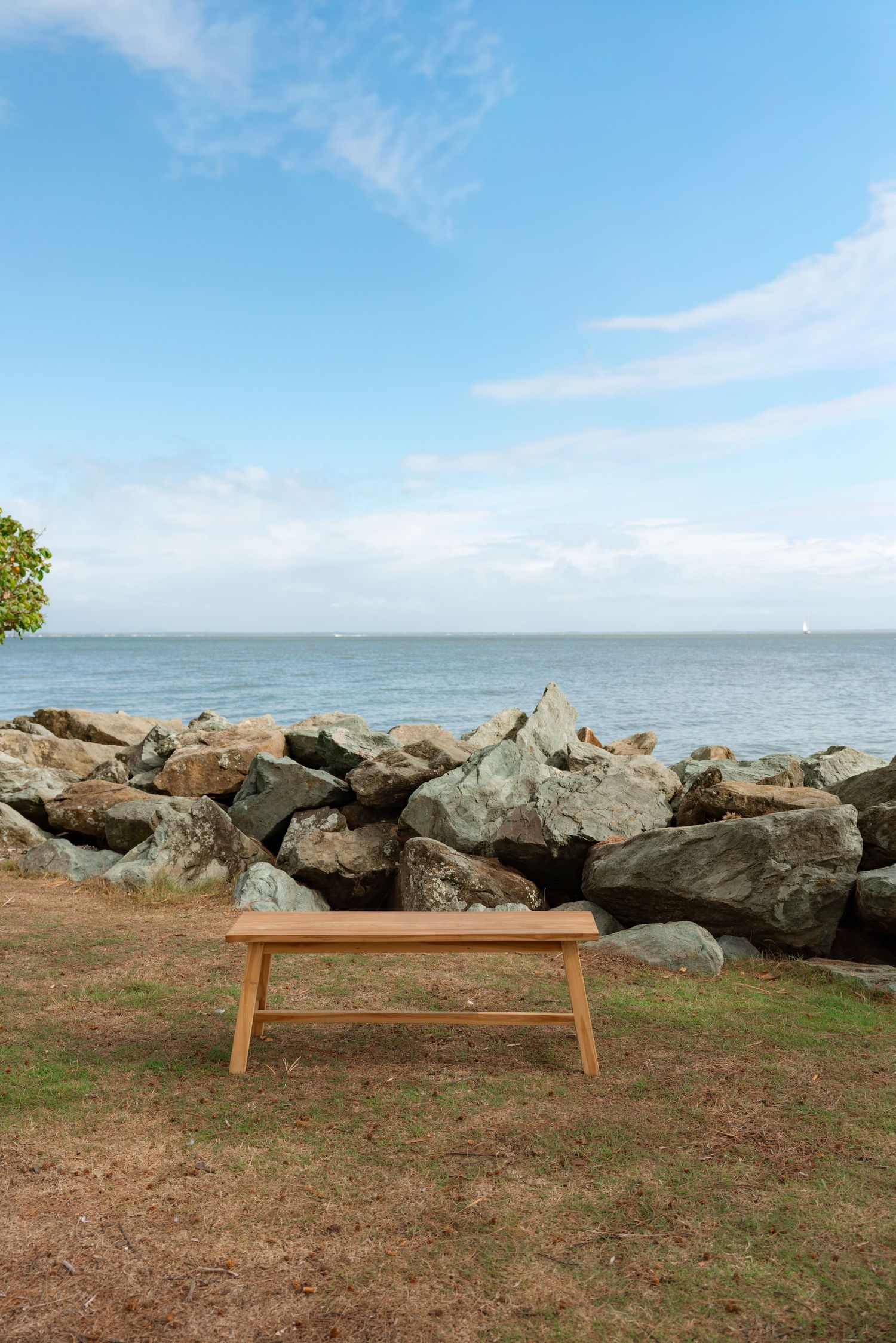 Wooden bench overlooking rocky coastline with ocean view under blue sky.