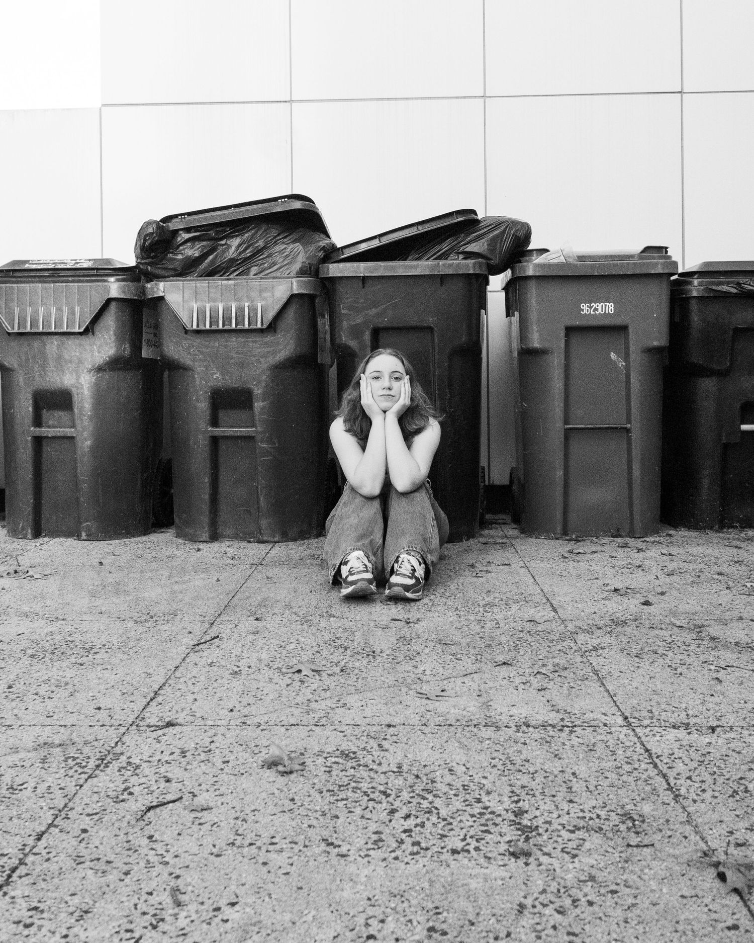 Woman sitting on the ground with garbage cans lined up behind