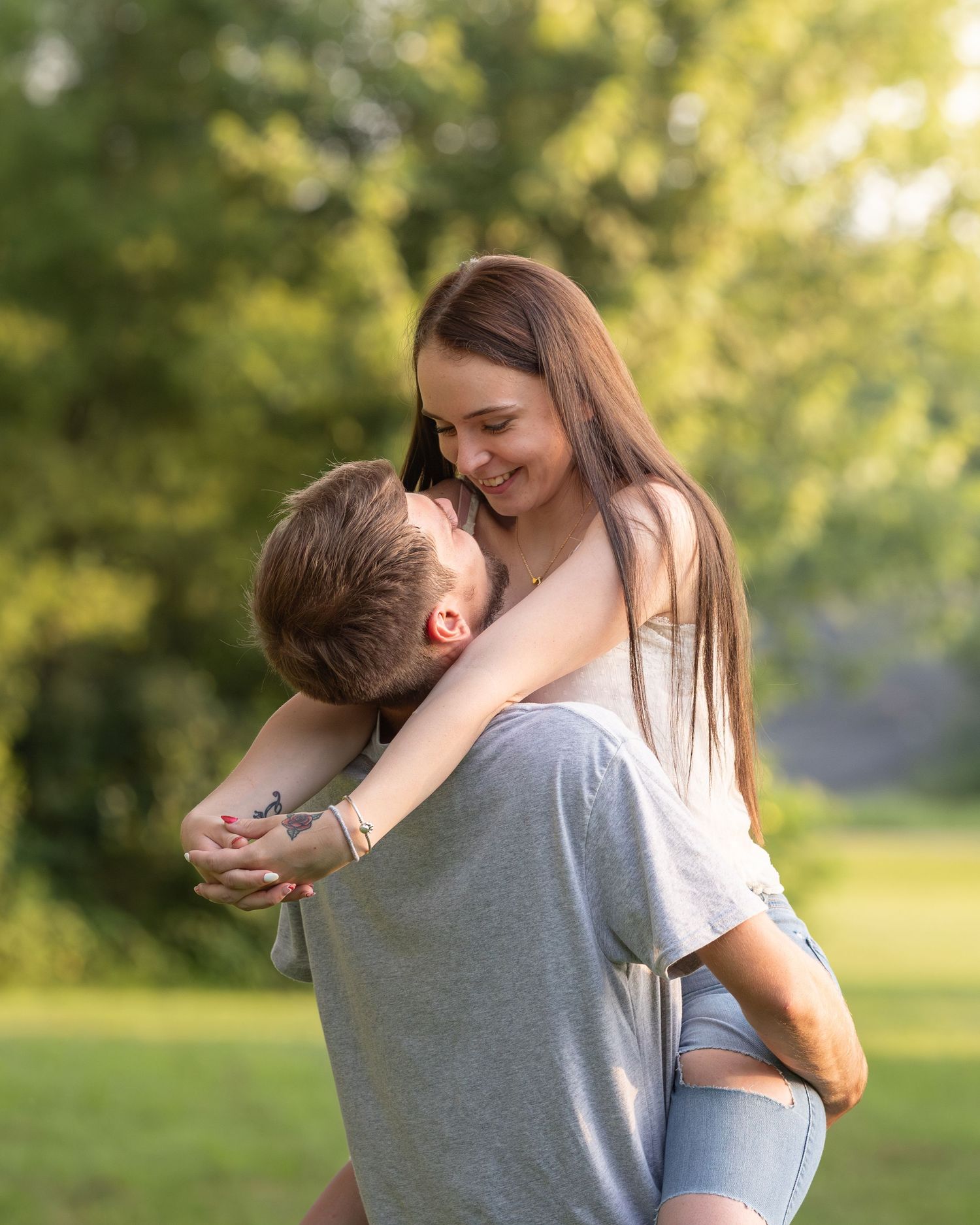 Couple sharing joyful embrace outdoors with man lifting woman in sunny green park.