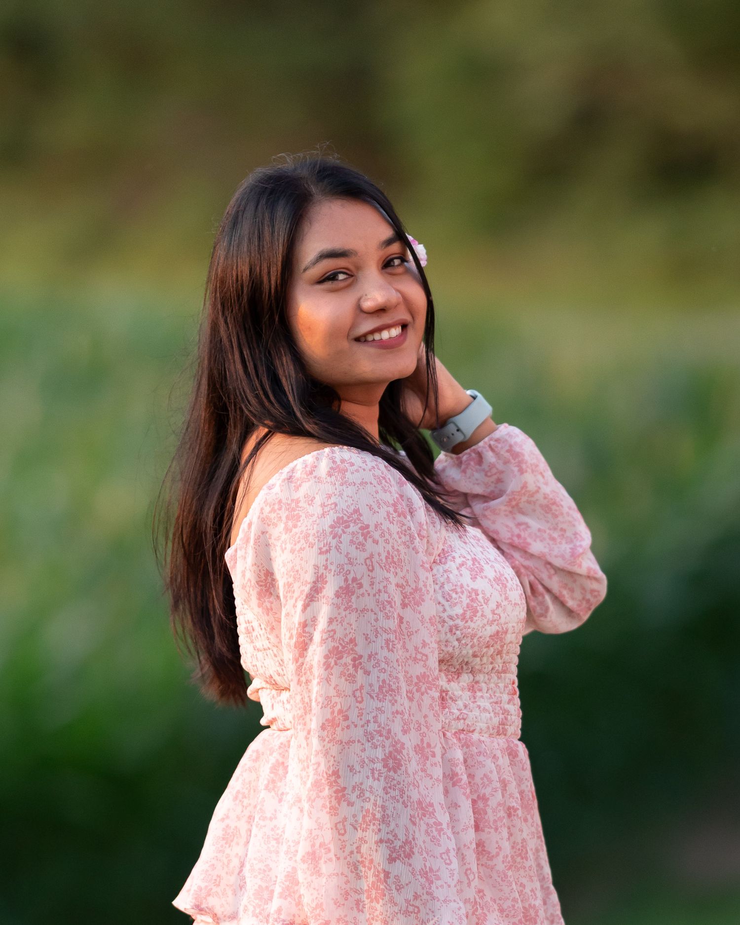 Smiling young woman in a floral pink dress posing outdoors in soft natural evening light.