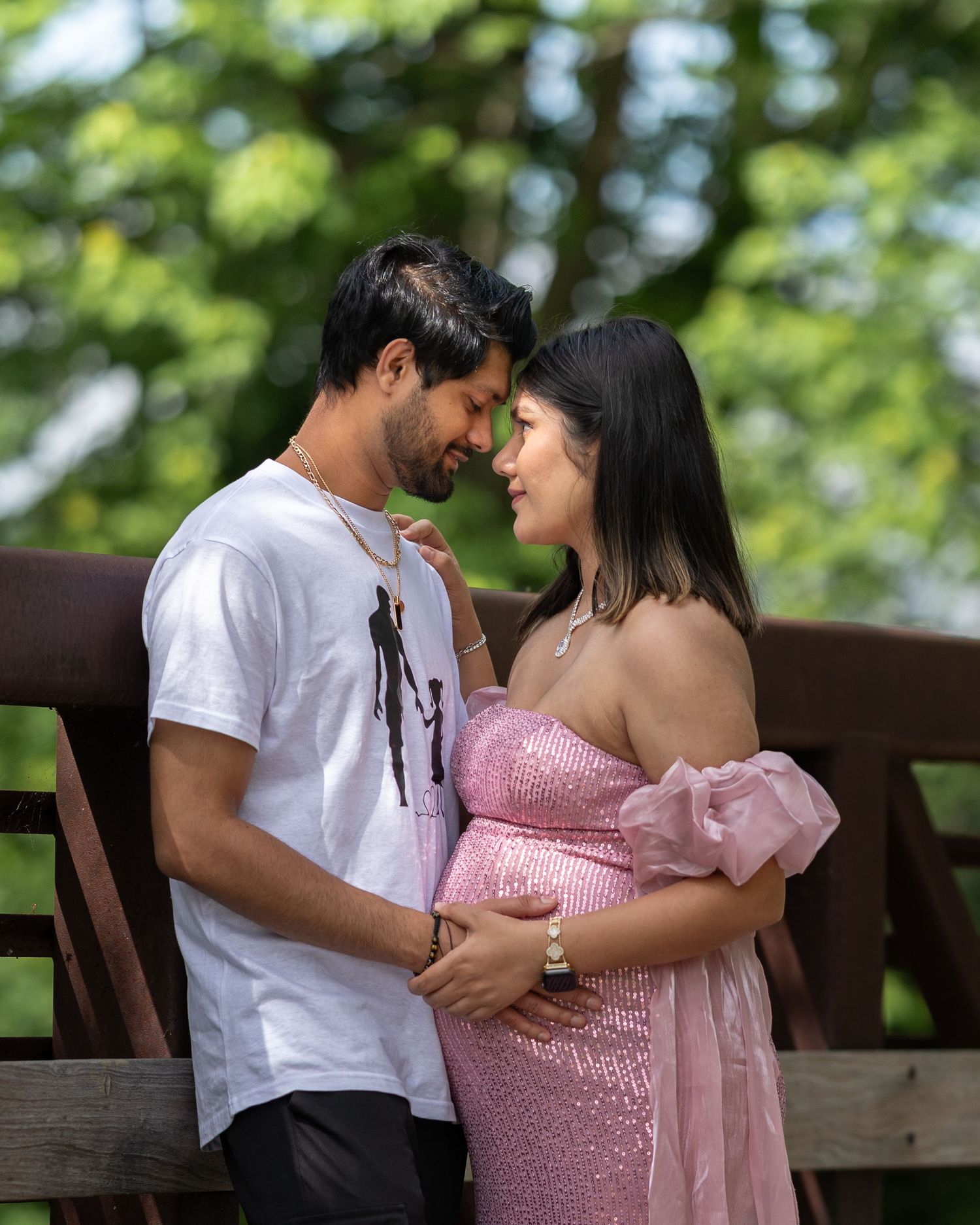Couple sharing an intimate moment on a wooden bridge during outdoor maternity photoshoot.