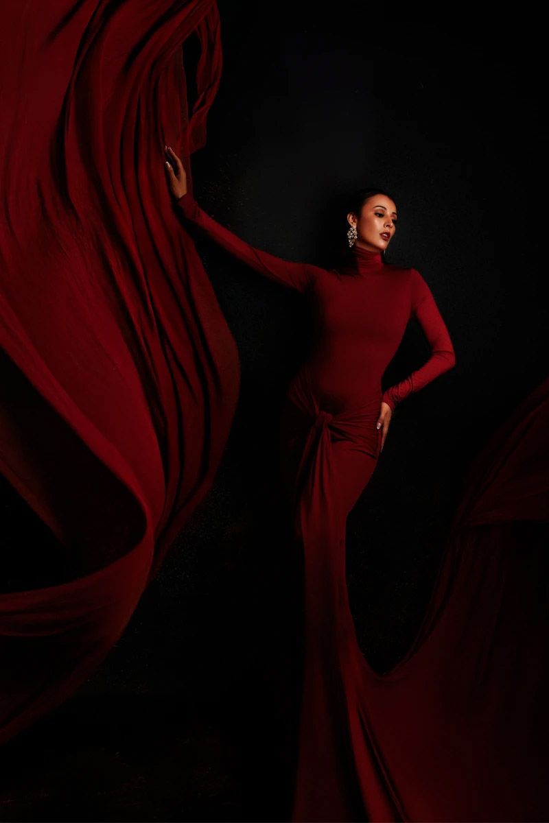 Dramatic fashion photo of a figure in flowing red dress against dark background.