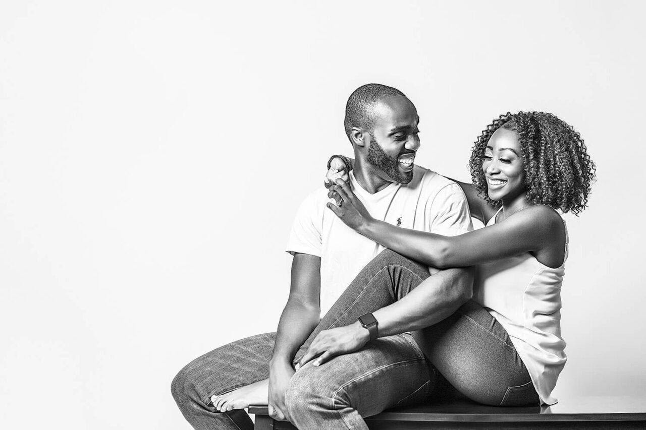 Loving couple in jeans and white shirts posing together against white studio backdrop.