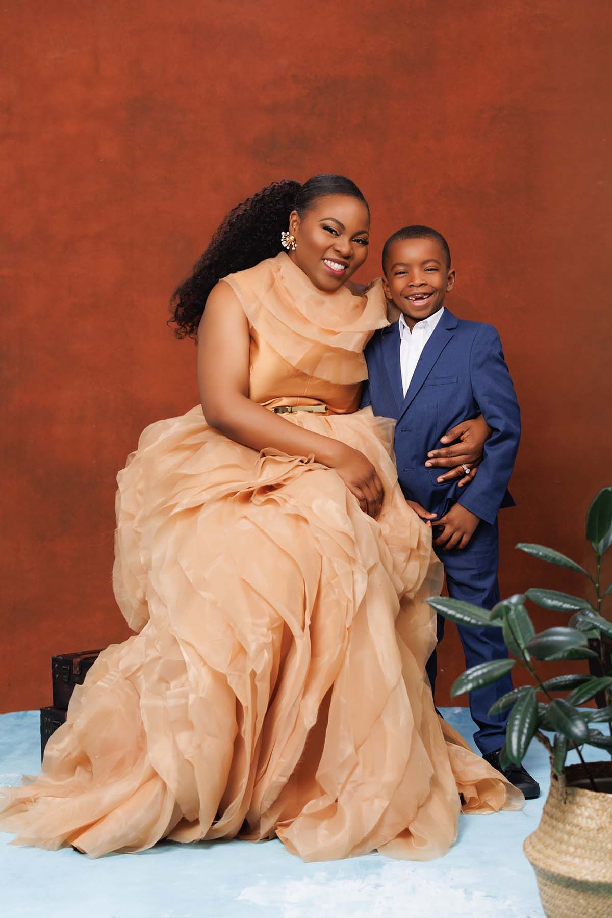 Elegant portrait against red backdrop featuring flowing peach gown and navy suit.