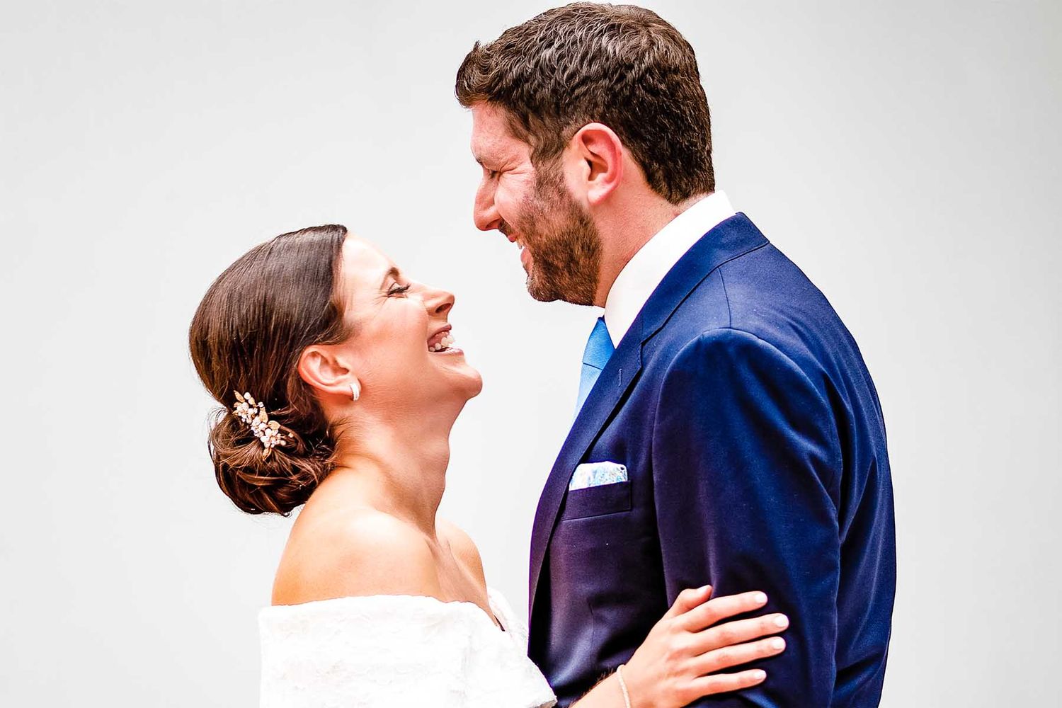 Romantic wedding portrait series showing couple in navy suit and white dress against light background.