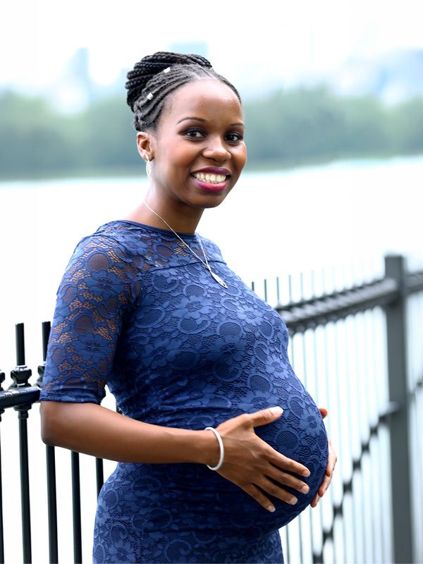 Person in navy blue lace dress poses elegantly by waterfront railing.