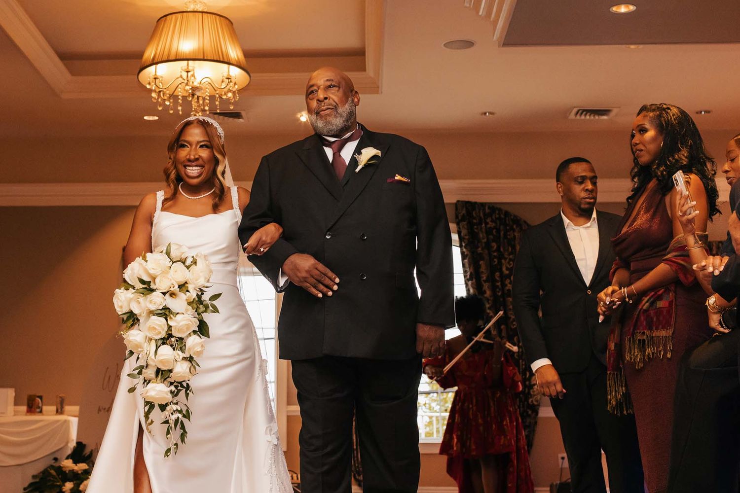 Wedding party dancing and celebrating in an elegant ballroom with chandelier lighting.