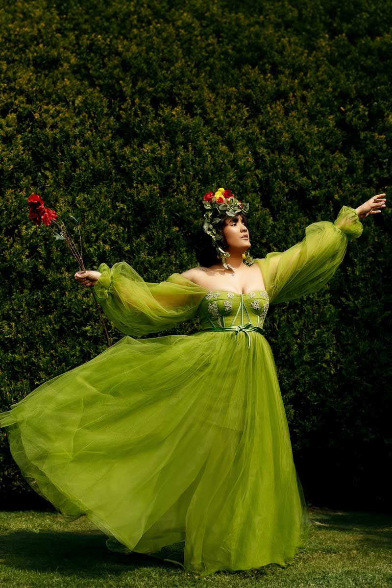 Model in lime green tulle gown twirling in garden setting with dramatic pose.