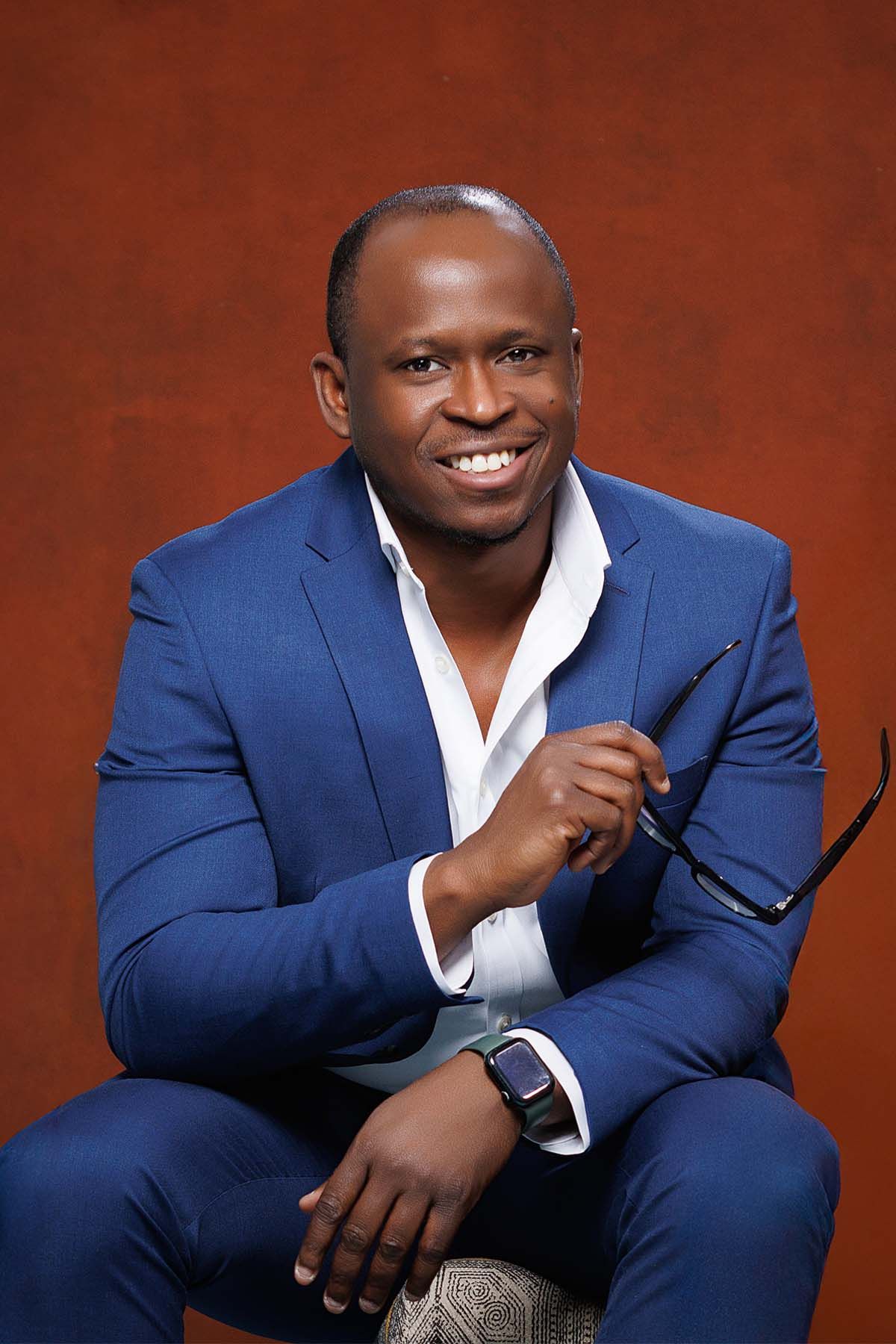 Professional portrait of man in navy suit smiling against brown background.